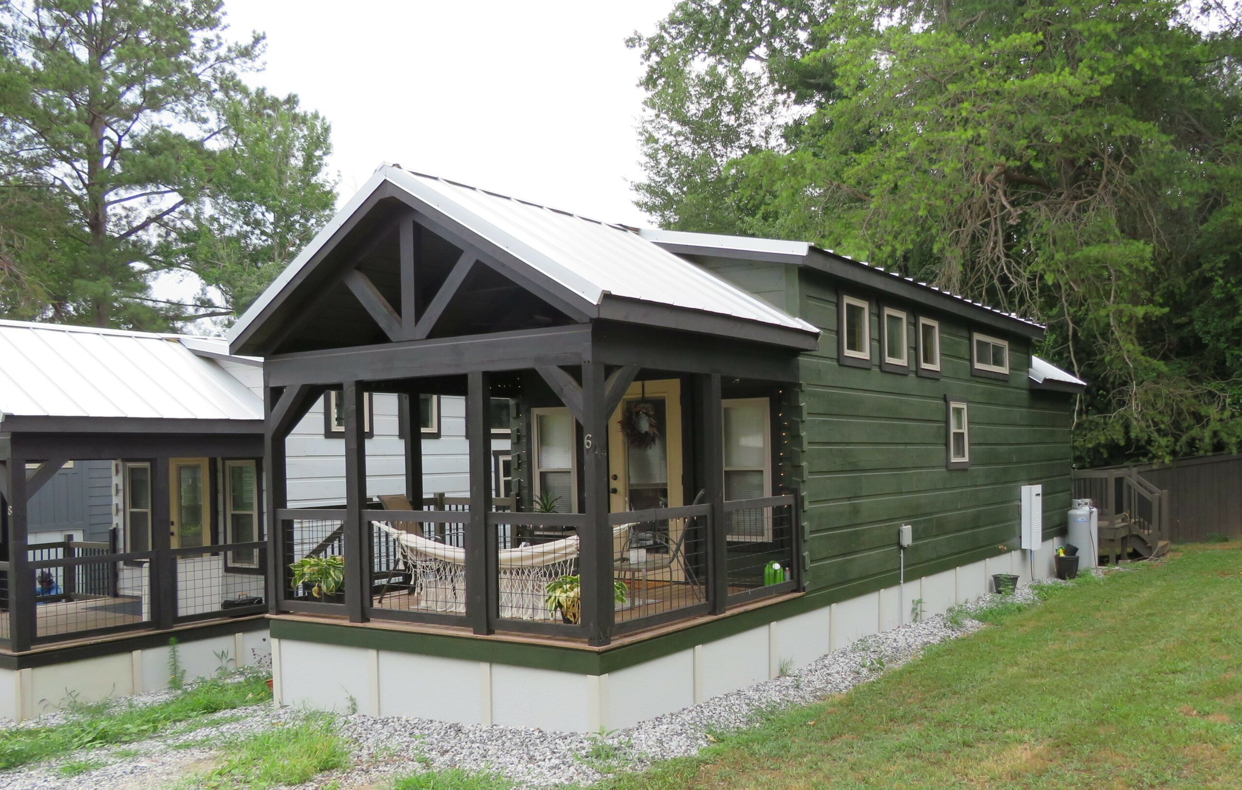Green house with a porch, surrounded by trees and grass, with a white roof and black trim.
