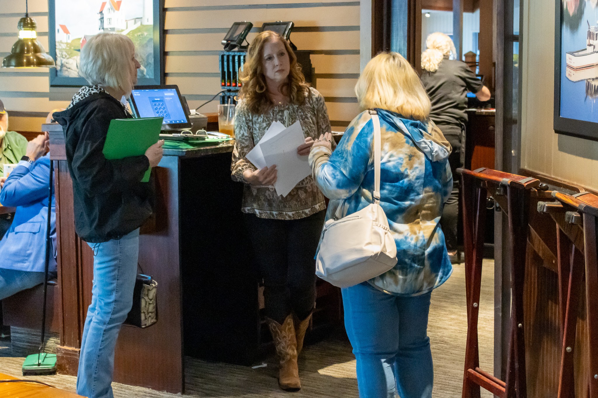Group of four women in a bookstore or library, engaging in conversation, with books and screens visible.