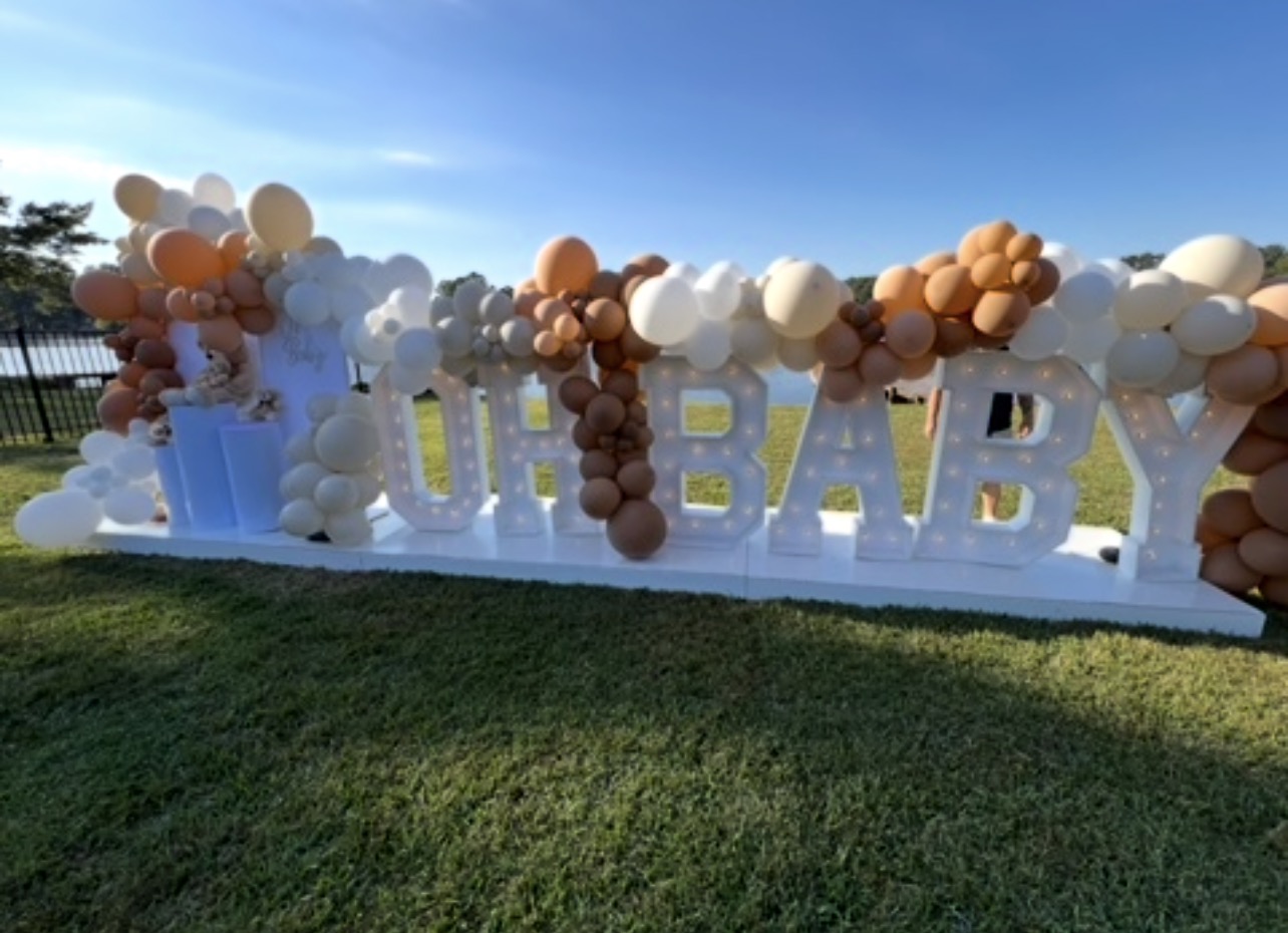 Decorative balloon arrangement with white, brown, and beige balloons on a grassy area under a blue sky.