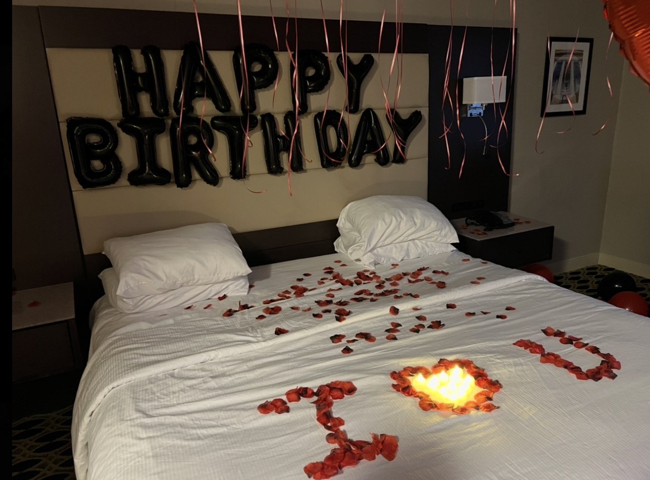 Bed with rose petals, birthday message, and a flame decoration, decorated for a birthday celebration.