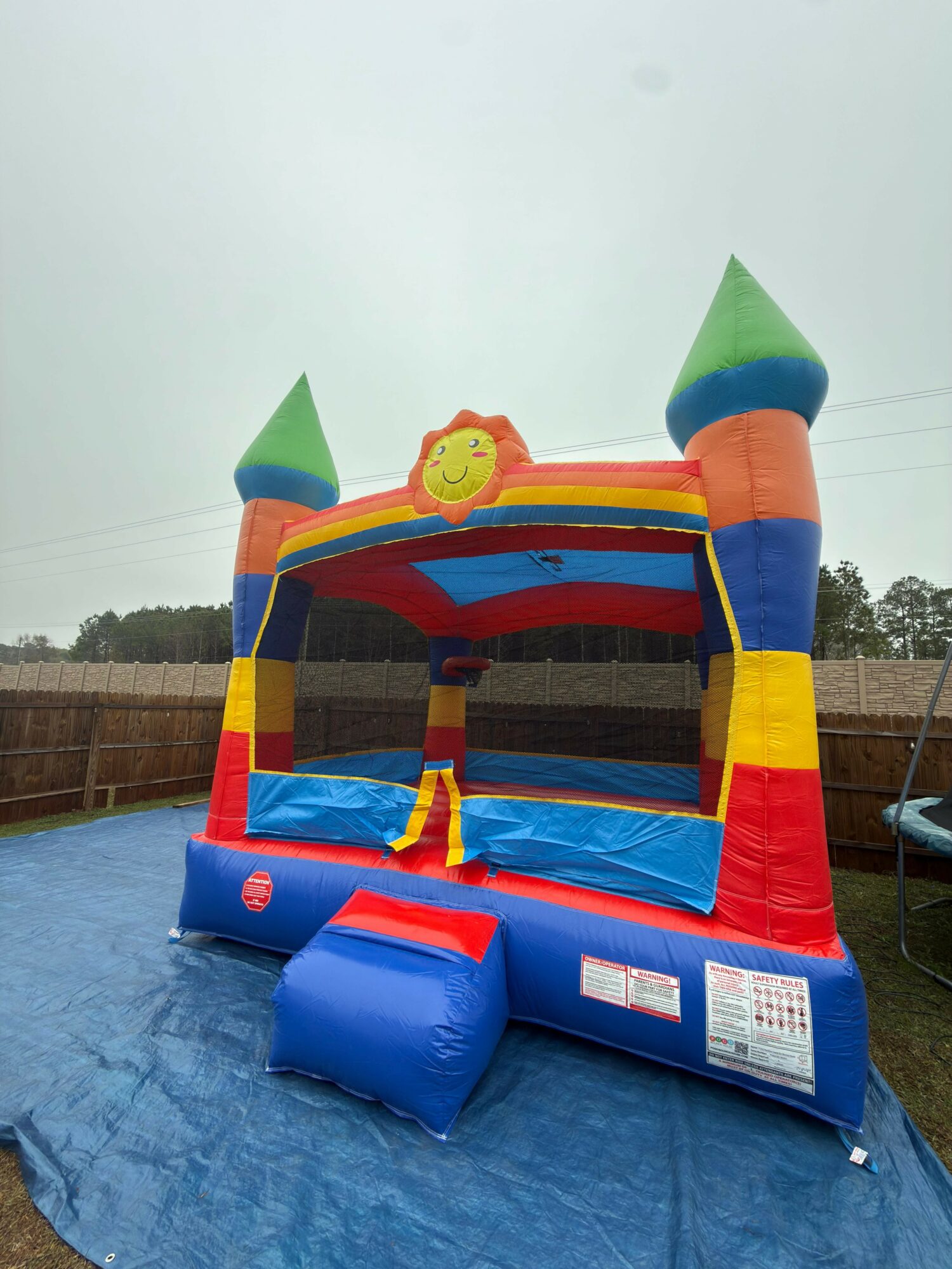 Colorful inflatable bounce house with towers and a sun decoration, set on a blue tarp outdoors.