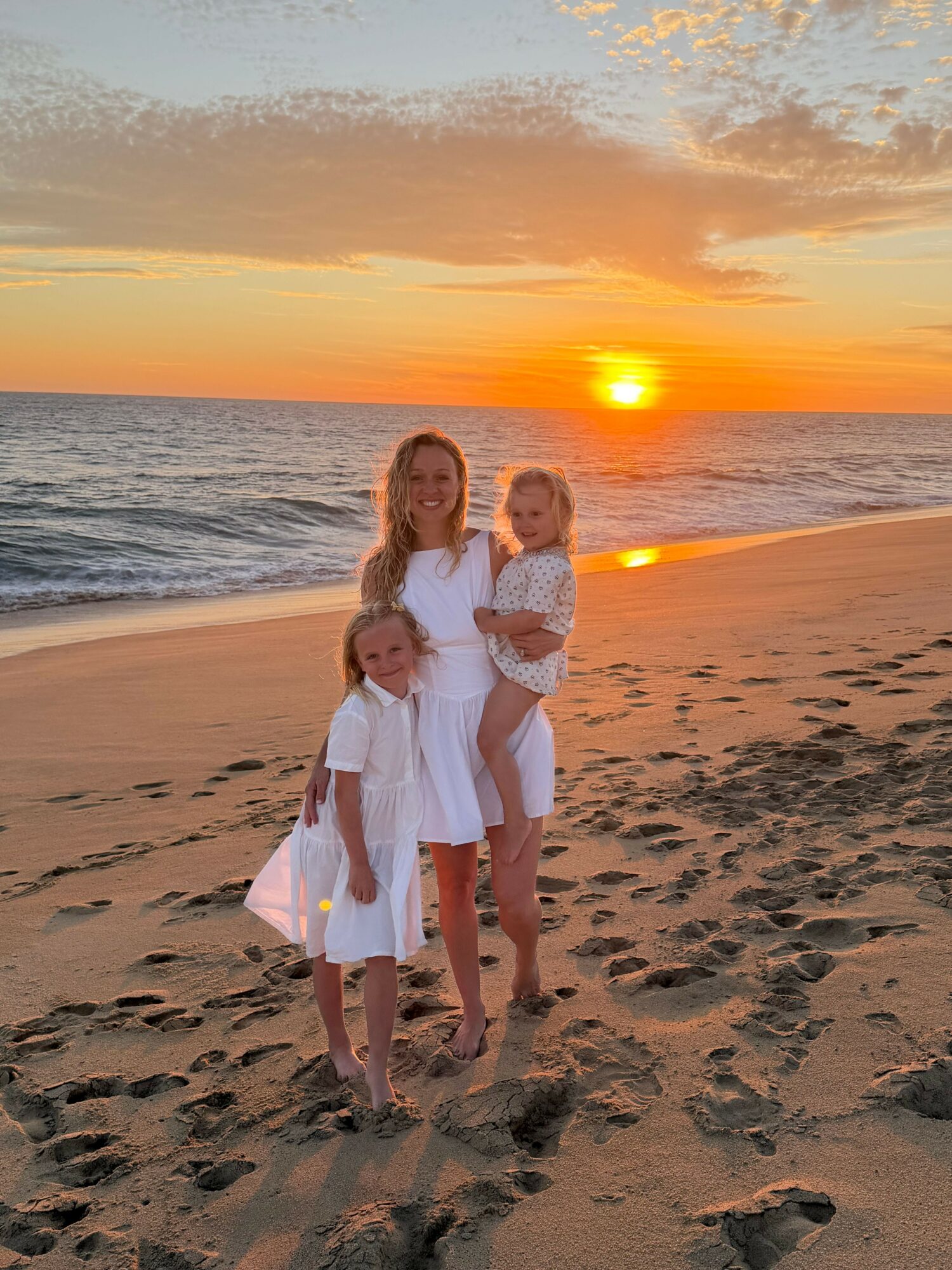 Three people standing on a beach during sunset, with ocean and sky in the background.