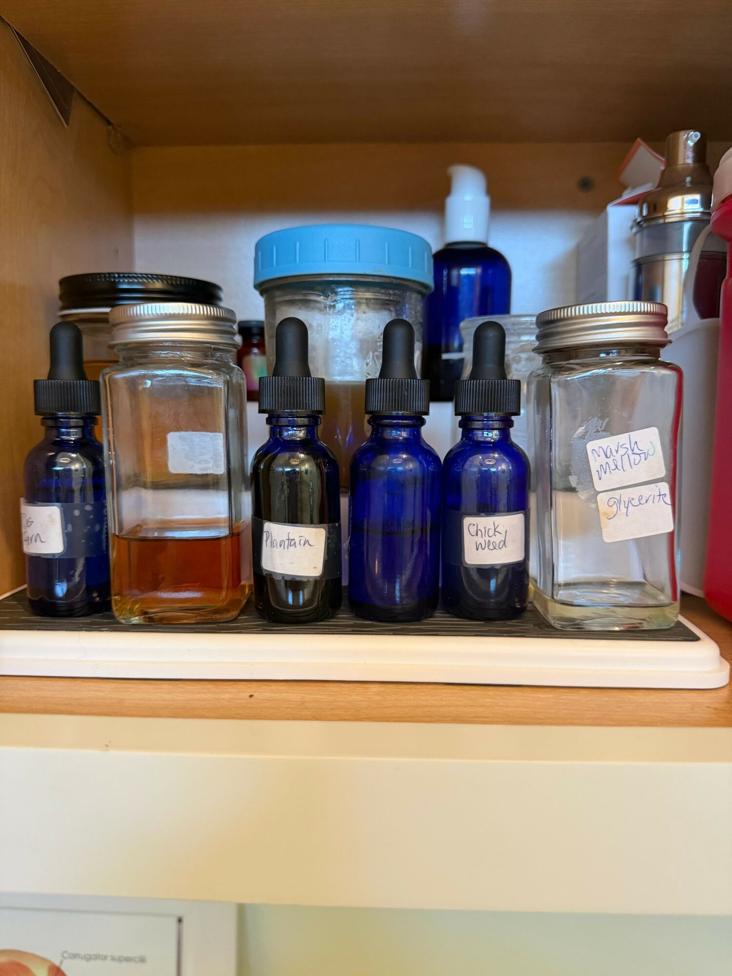 Shelf with glass bottles, jars, and containers, some with labels, on a wooden surface inside a cabinet.