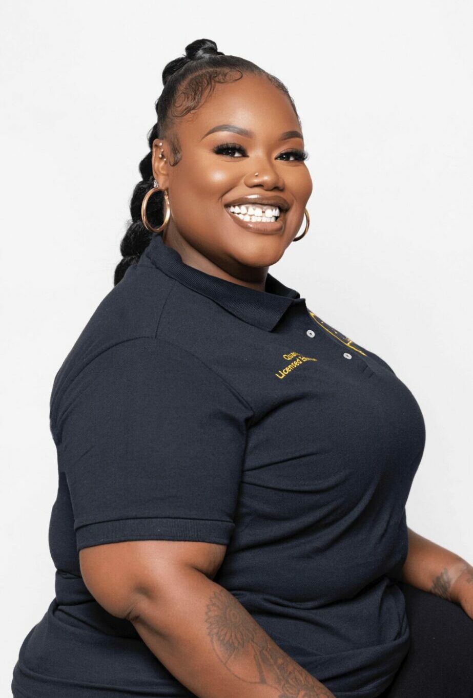 Smiling woman with braided hair, wearing a navy polo shirt and hoop earrings, against a white background.