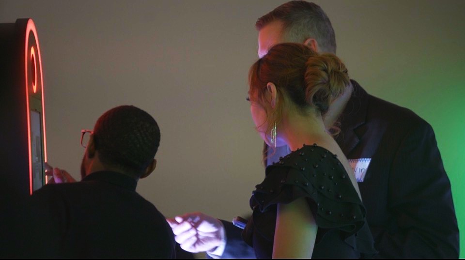 Three people gathered around a glowing screen or device, with one person showing something to the others, in a dim setting.