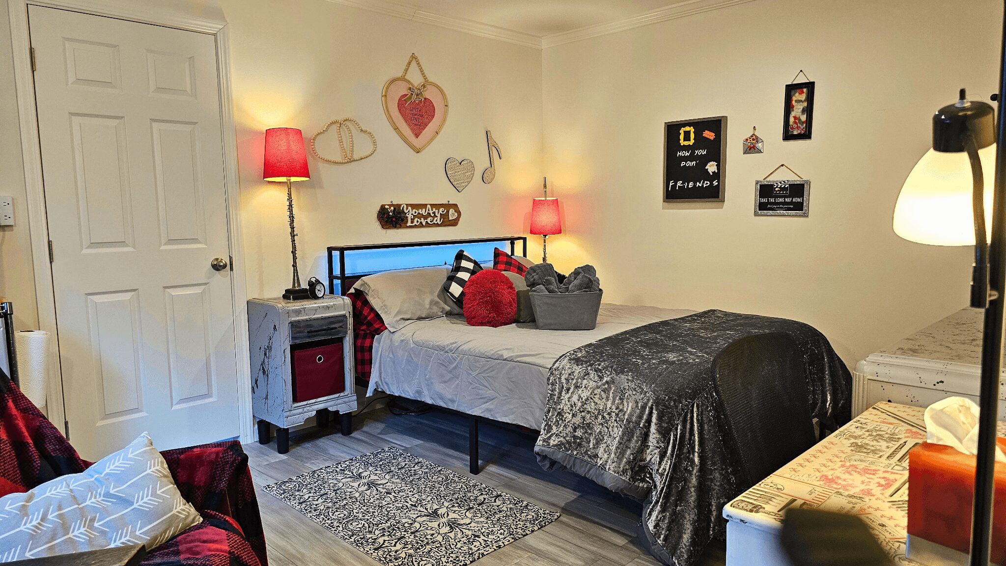 Bedroom with bed, nightstand, lamps, wall decorations, and a chair, illuminated by warm lighting.