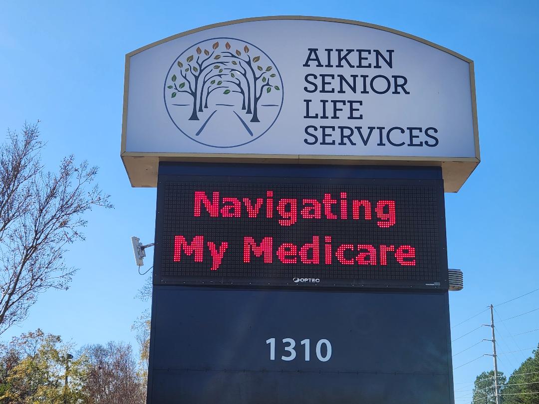 Sign for Aiken Senior Life Services with a digital display reading Navigating My Medicare, and the address 1310.