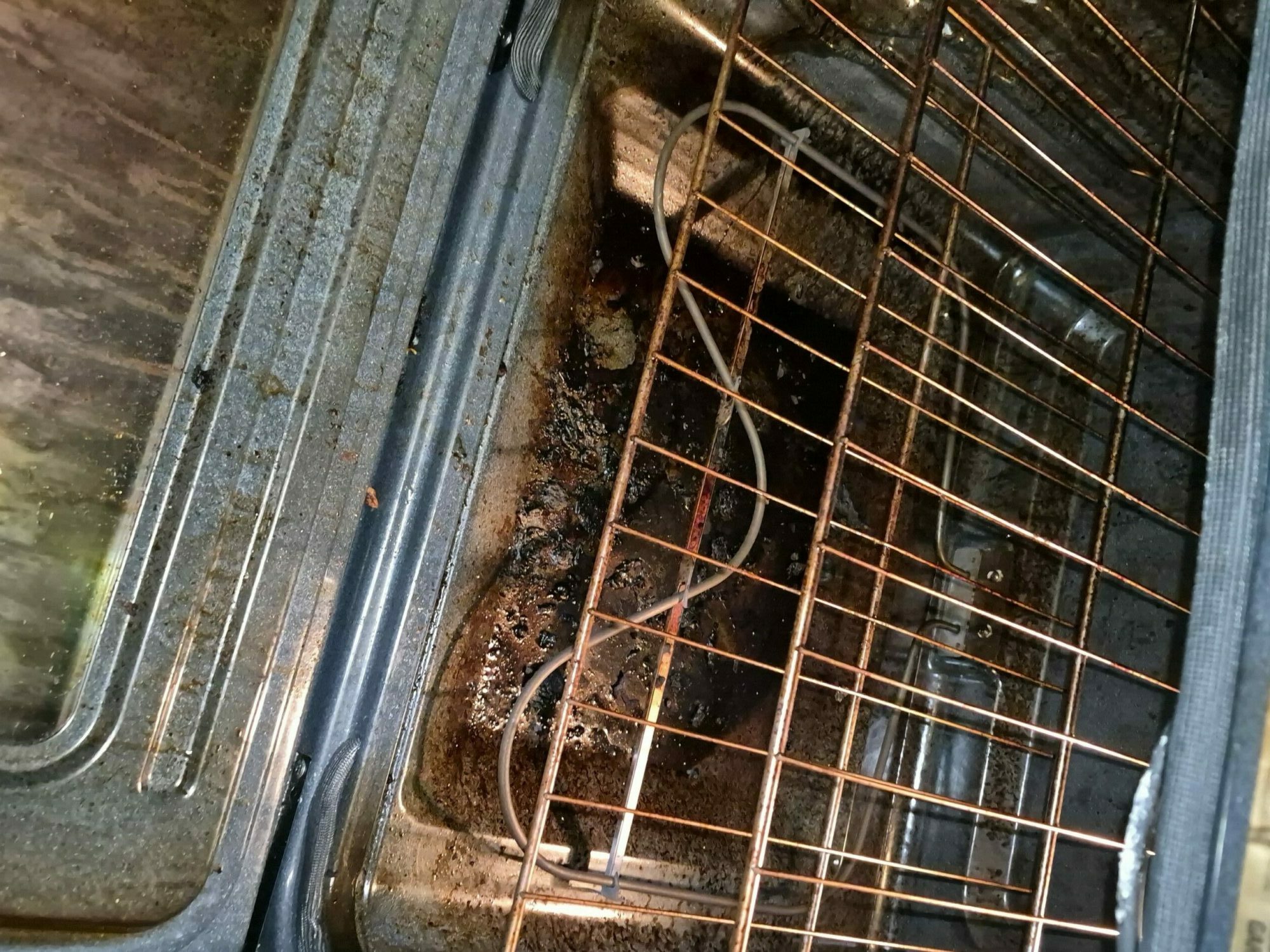 Oven with burnt food and a metal rack inside, viewed from the side.