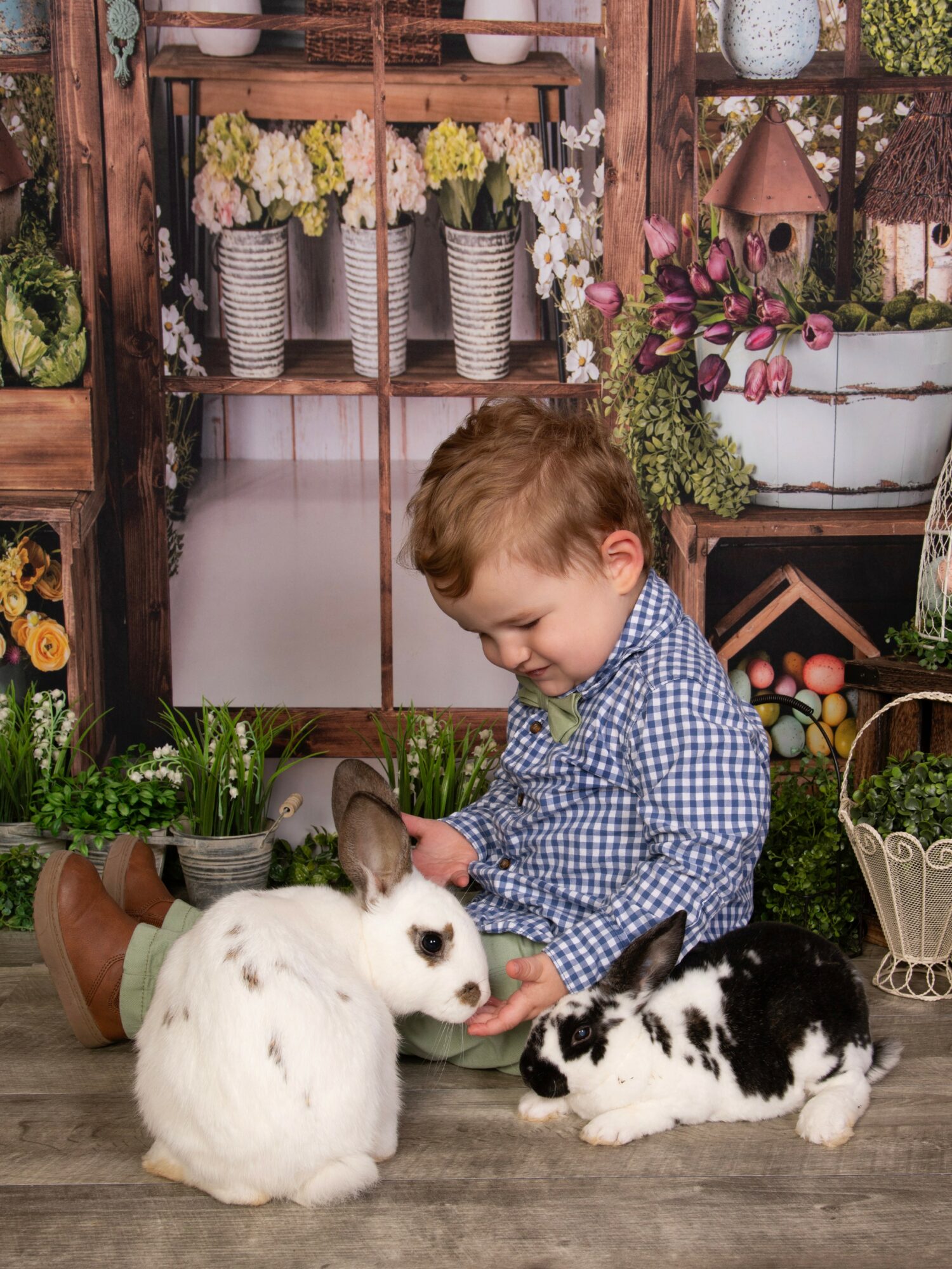 Child sitting on floor with two rabbits, one white and one black and white, in a floral and garden-themed setting.