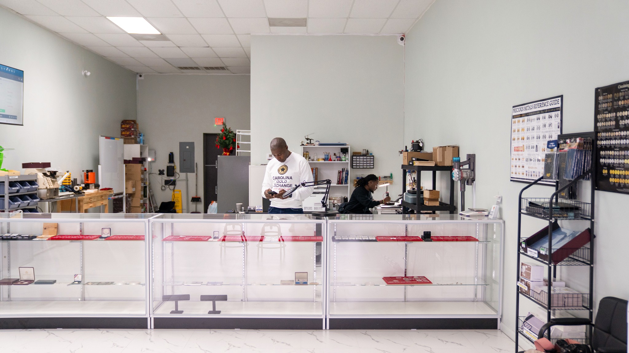 People working behind a counter in a store or office with shelves and equipment.
