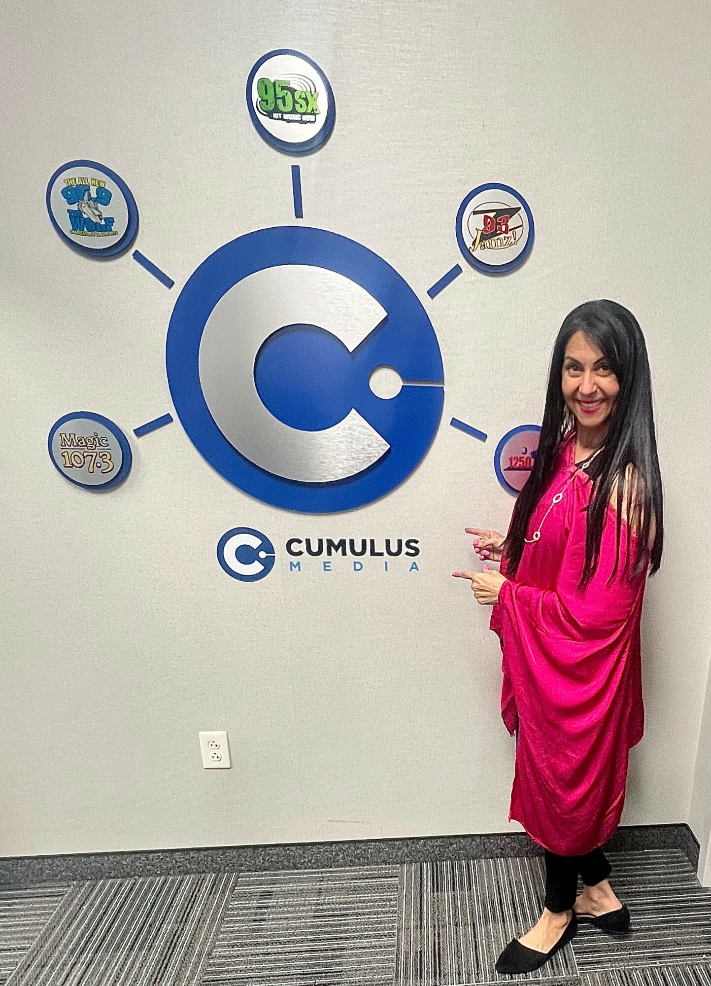 Woman in pink dress standing next to a wall with a large circular logo and smaller icons.