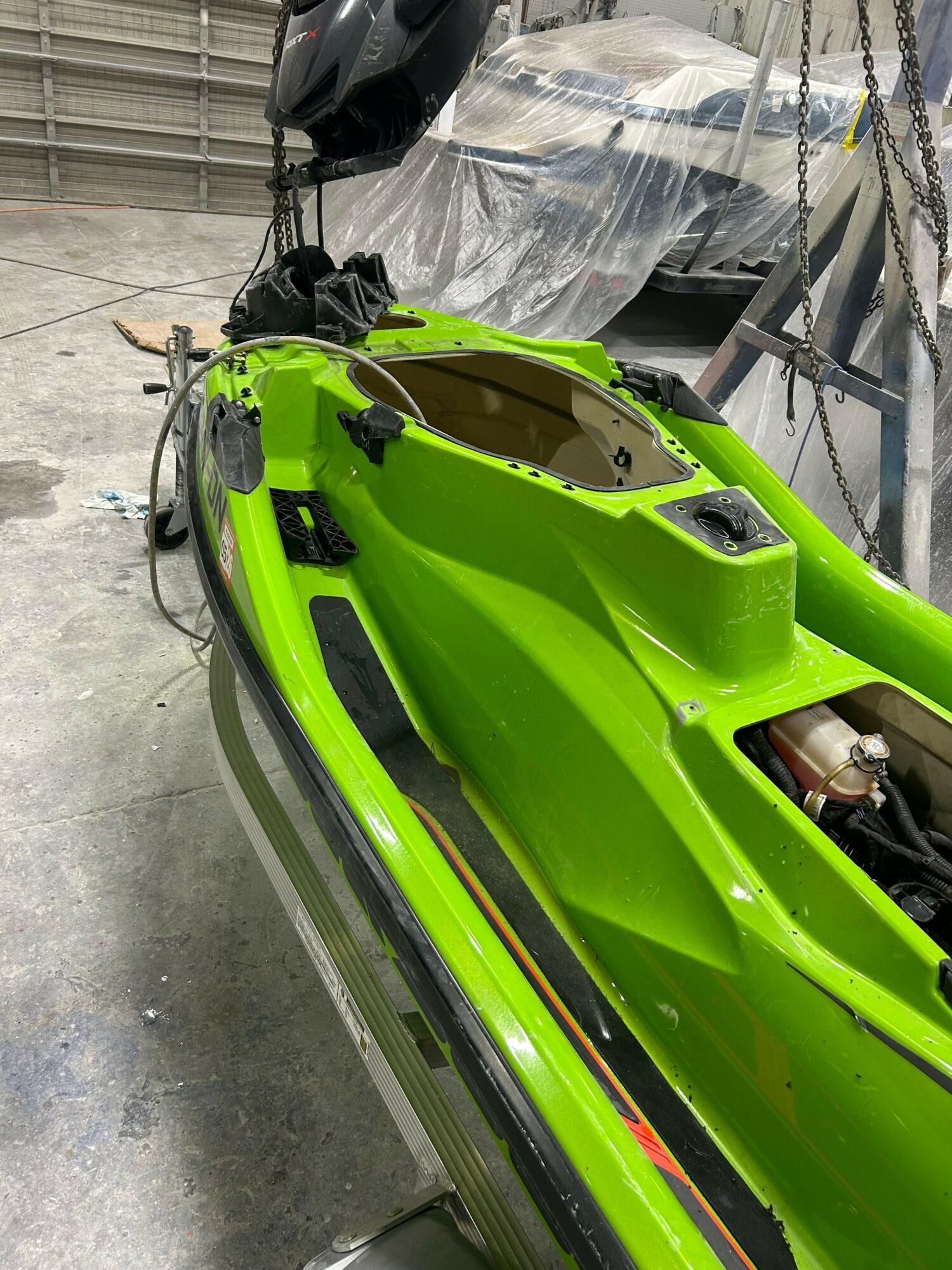 Bright green kayak with black handles and hardware, inside a workshop with a covered vehicle in the background.