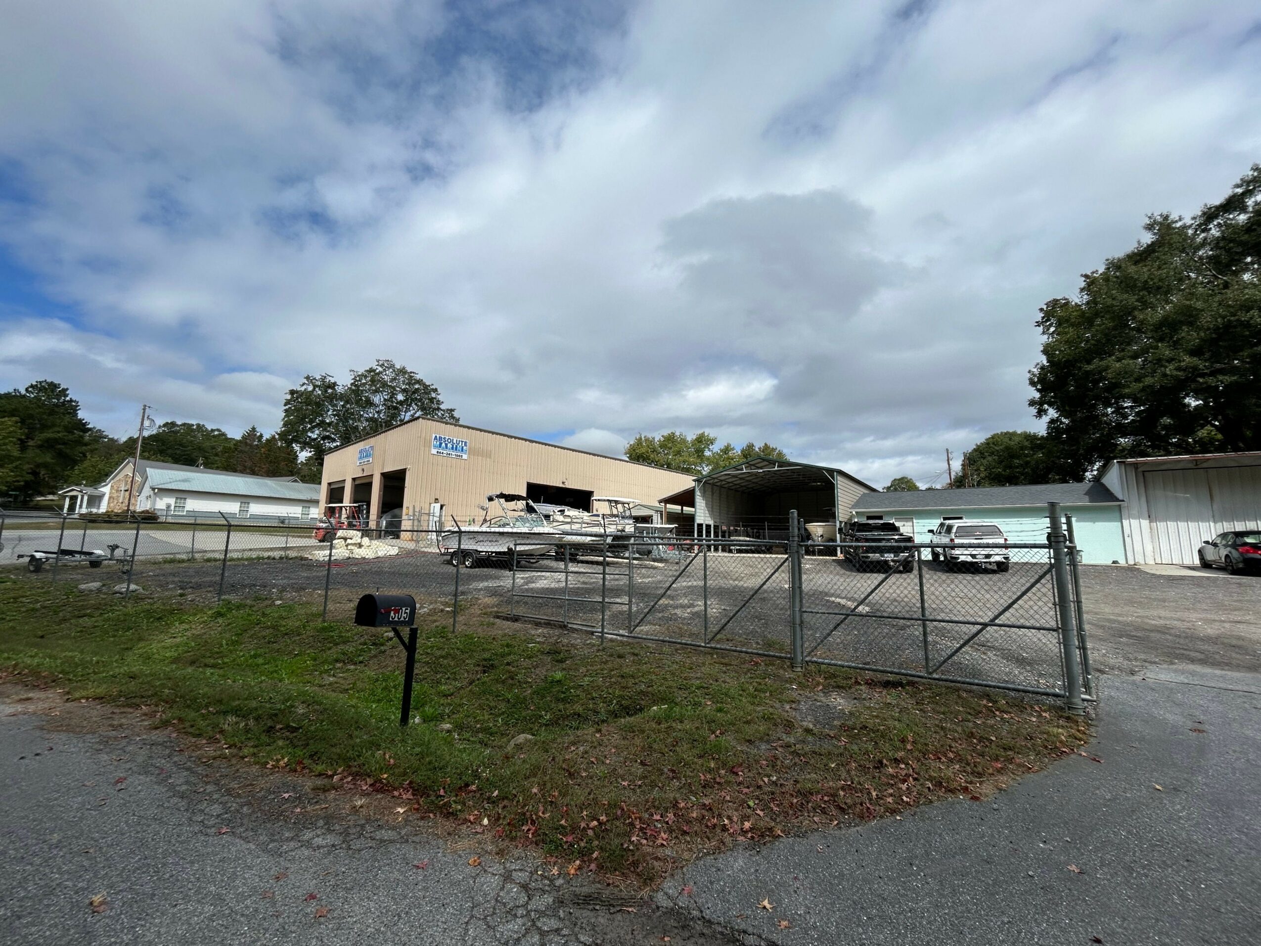 Industrial building with parked cars and a chain-link fence, under a partly cloudy sky.