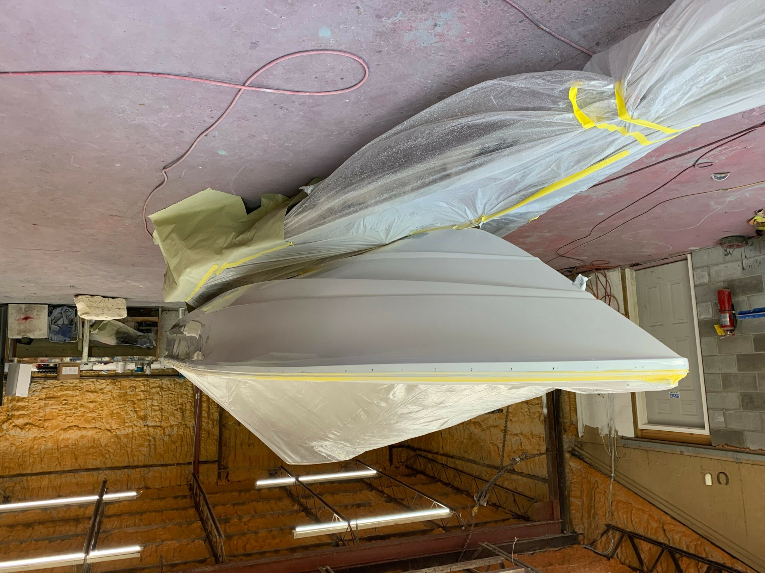 Object wrapped in plastic and tape on a pink floor with a wooden wall and metal railing nearby.