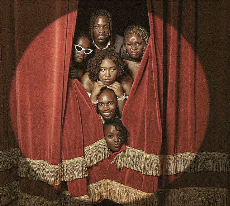 Six people peeking through red theater curtains with gold trim, posing together behind the curtains.