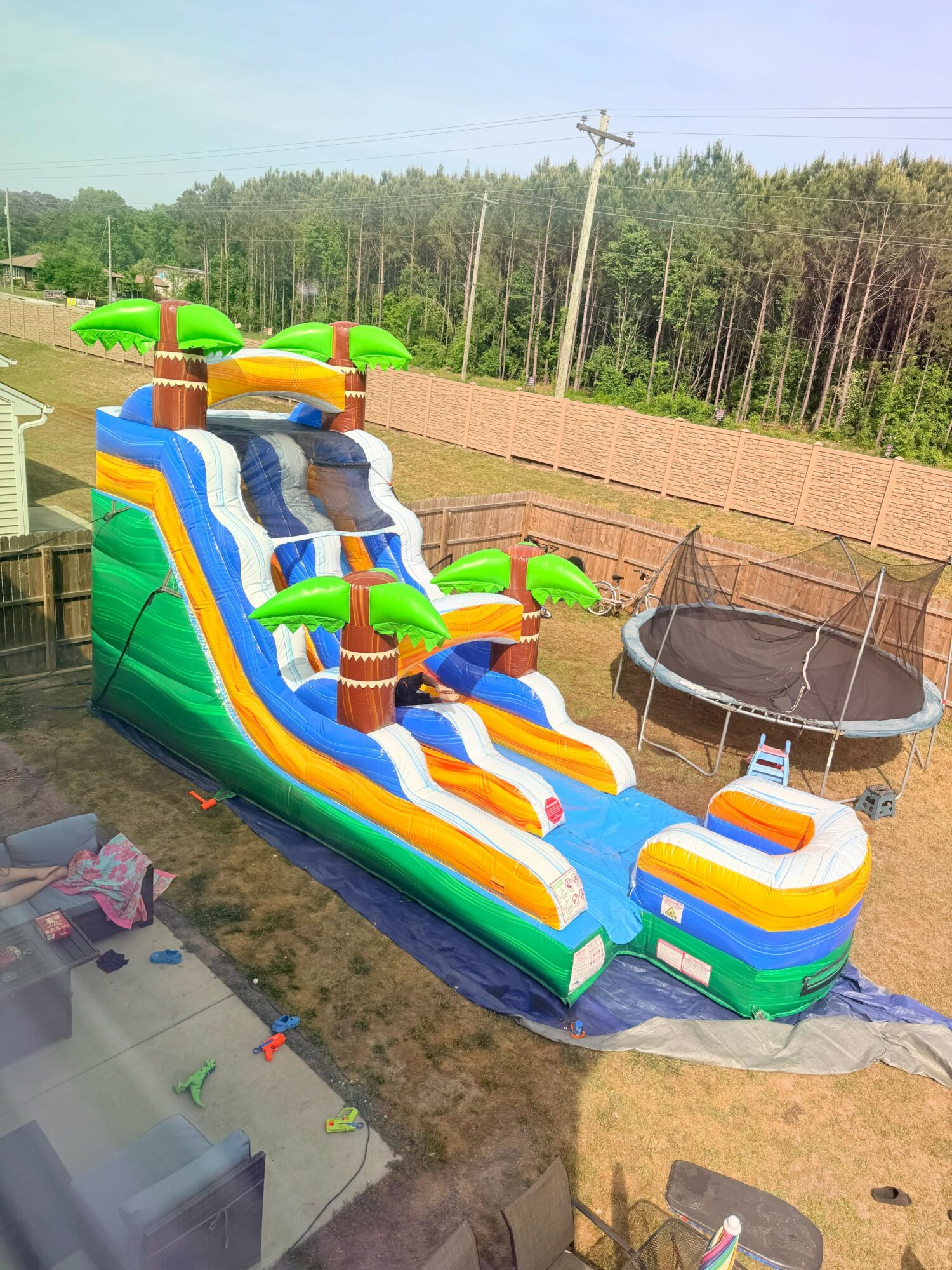 Colorful inflatable water slide with multiple slides and a pool at the bottom, set up outdoors on grass and tarp.