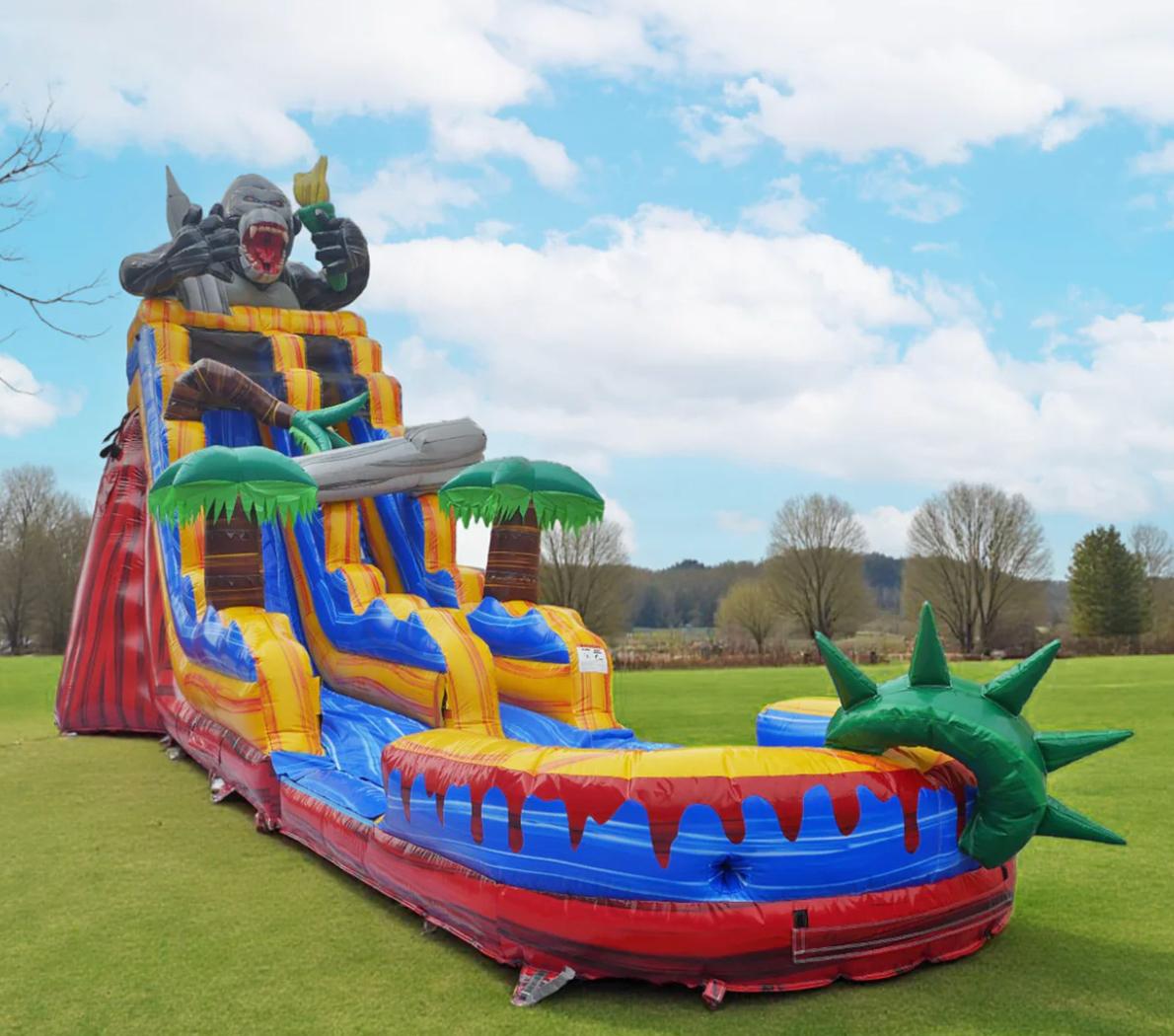 Large inflatable water slide with a dragon head at the top, multiple slides, and palm trees, set outdoors on grass.