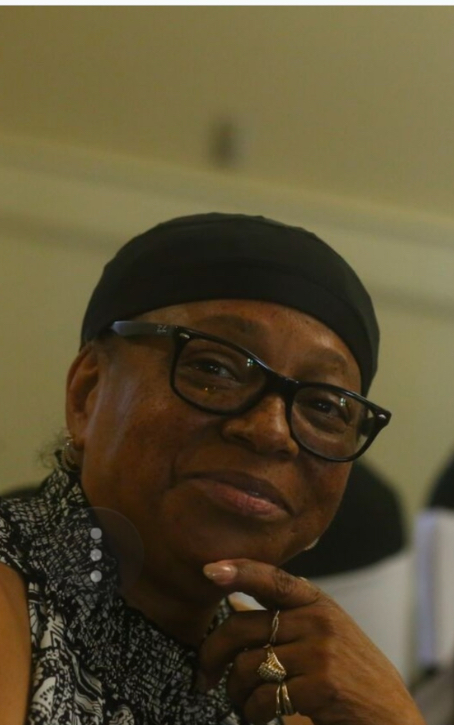 Woman wearing glasses and a head covering, resting her chin on her hand, indoors.