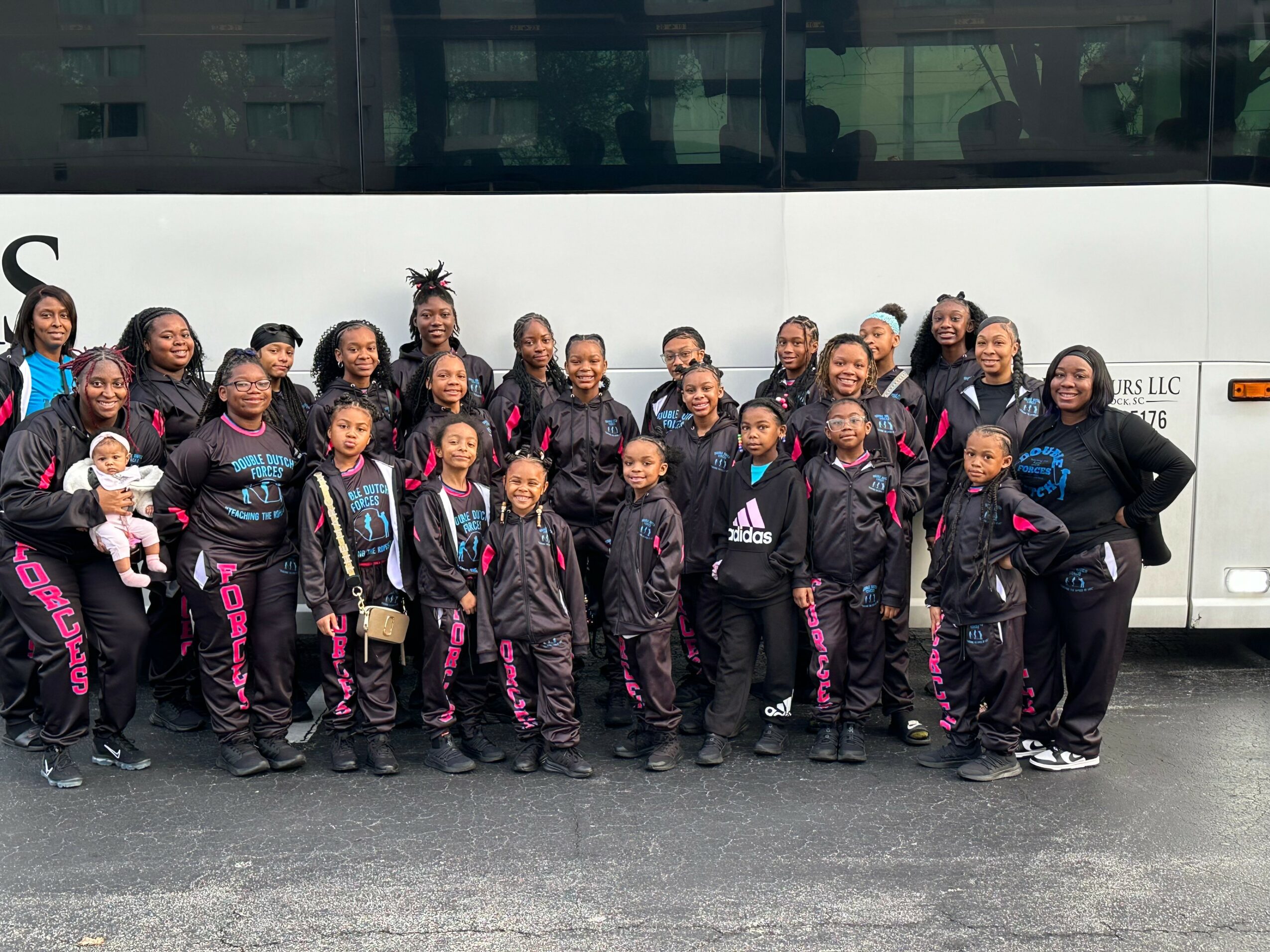 Group of children and adults standing in front of a bus, smiling and posing for a photo.