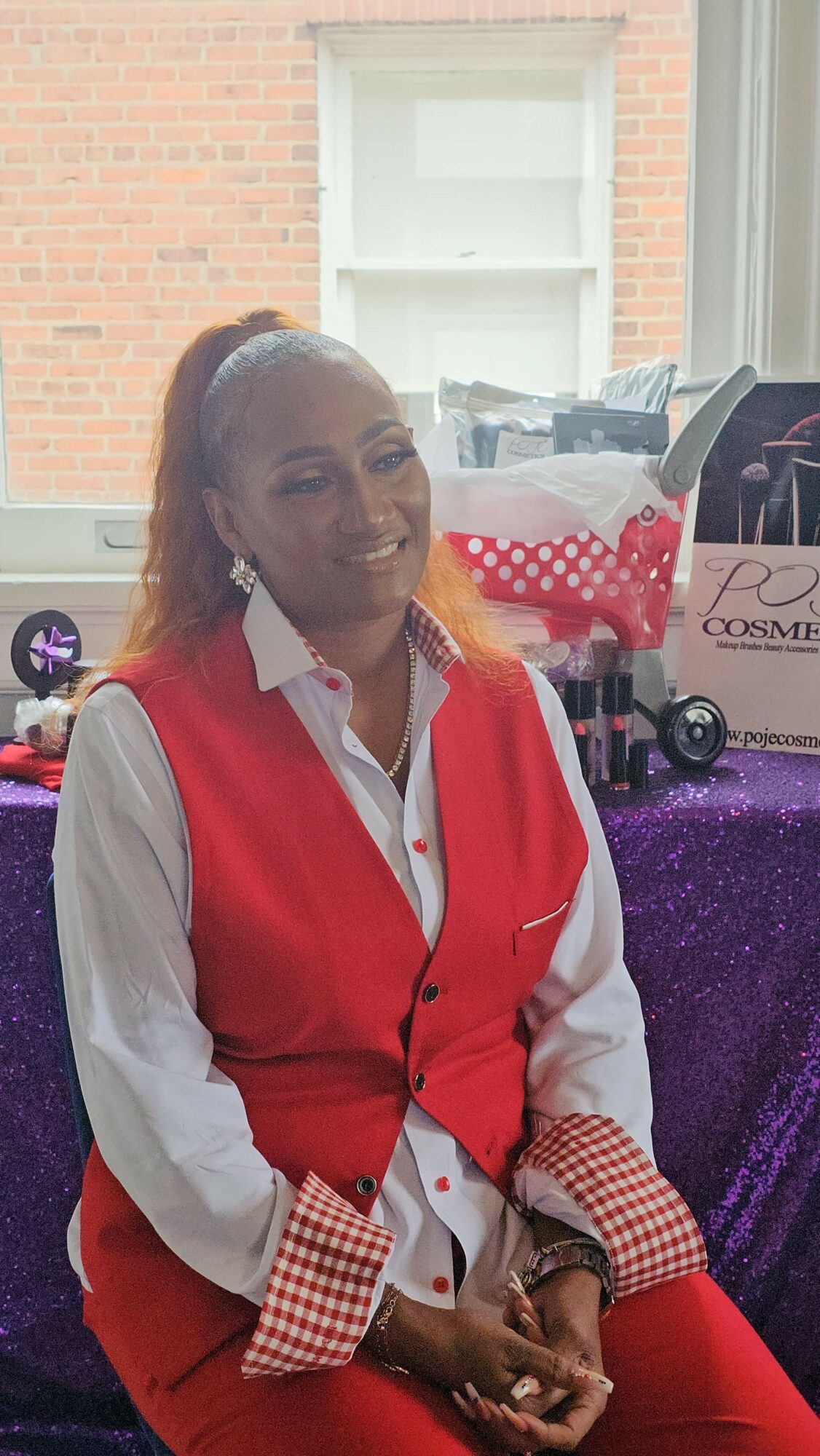 Person with long hair wearing a red and white jacket, sitting at a table with a purple tablecloth, talking on a phone.