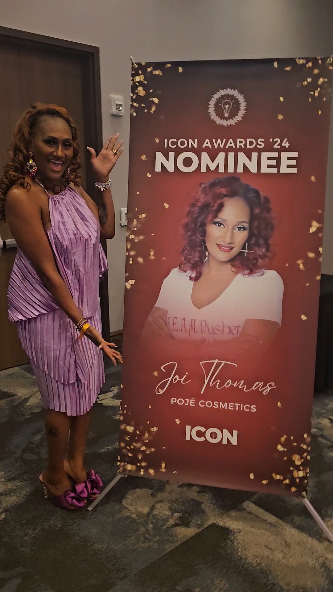 Woman in purple dress standing next to a nominee sign for Jo Thompson at ICON Awards 2024, smiling and waving.