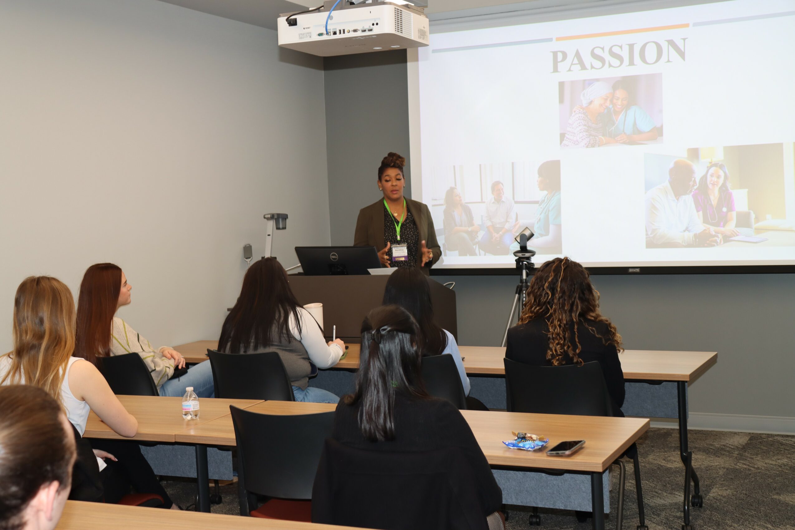 Woman presenting to a group of people in a conference room with a large screen displaying a presentation titled 'PASSION'.