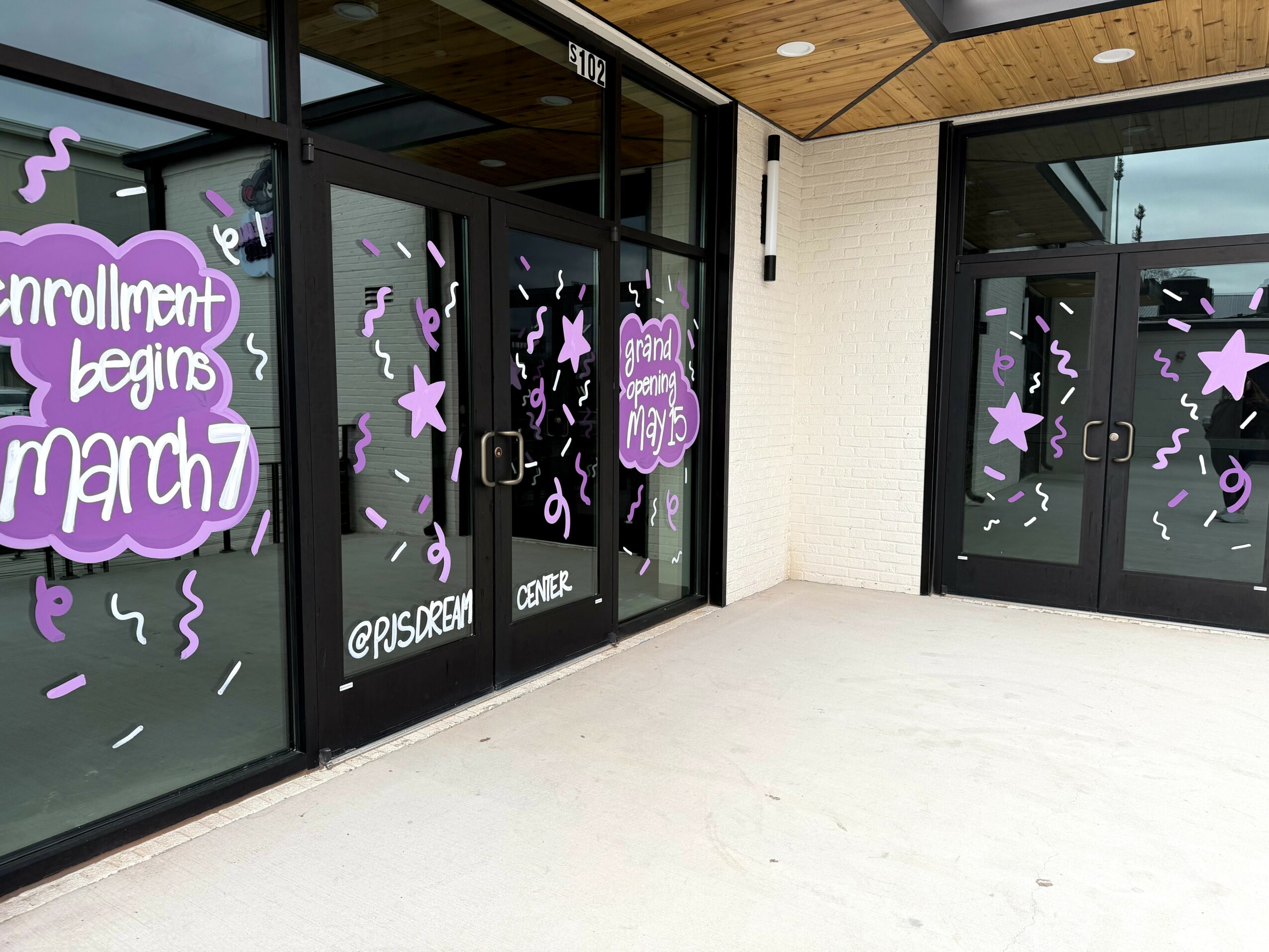 Glass doors with purple and white decorations for enrollment event, including stars and text, outside a building.