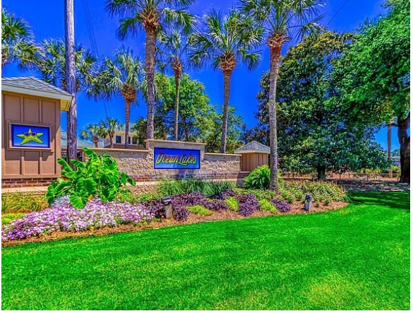 Lush green lawn with colorful flower beds, palm trees, and a sign reading 'Dream Lake' in a sunny outdoor setting.