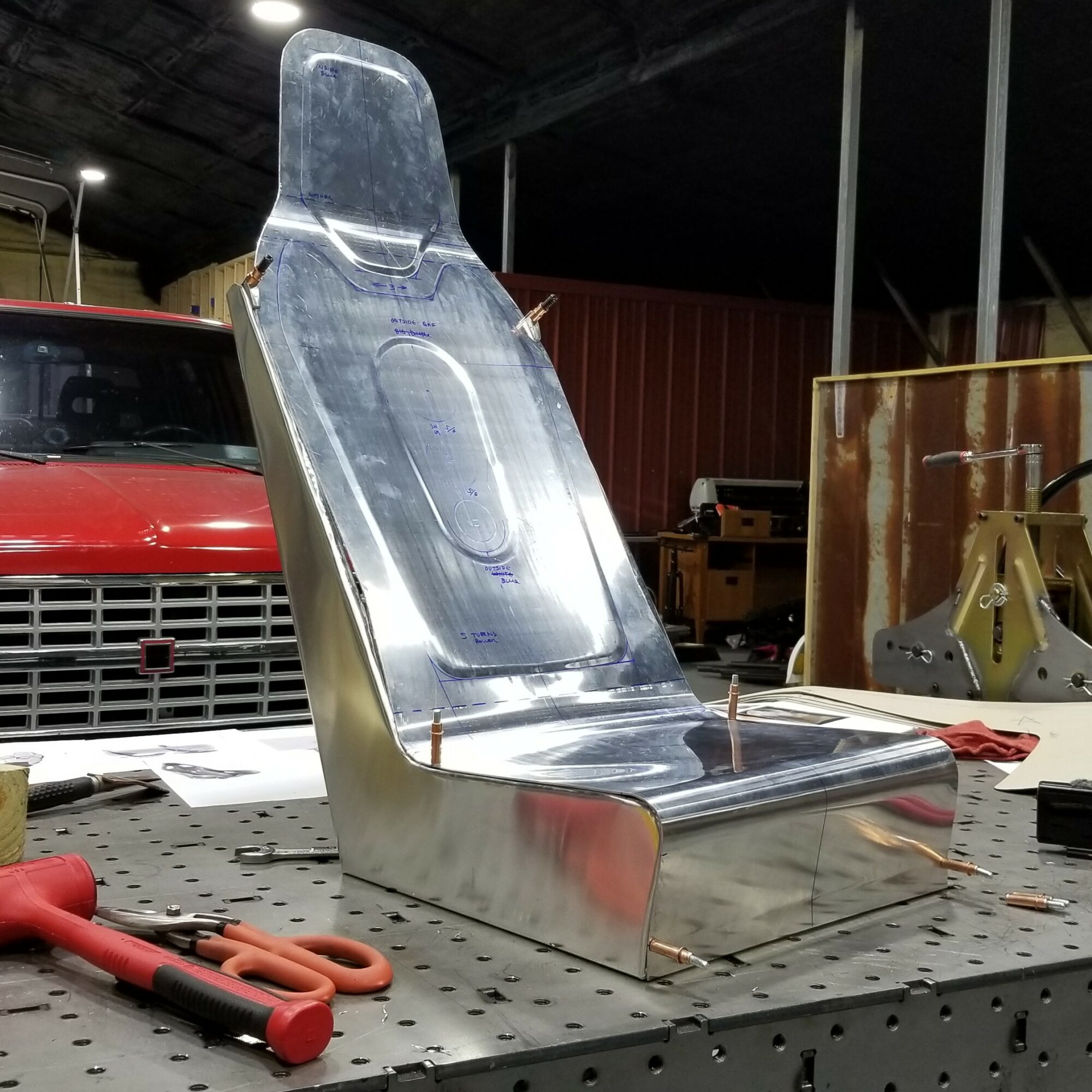 Metal chair with high backrest and seat, placed on a workbench in a workshop, with tools nearby.