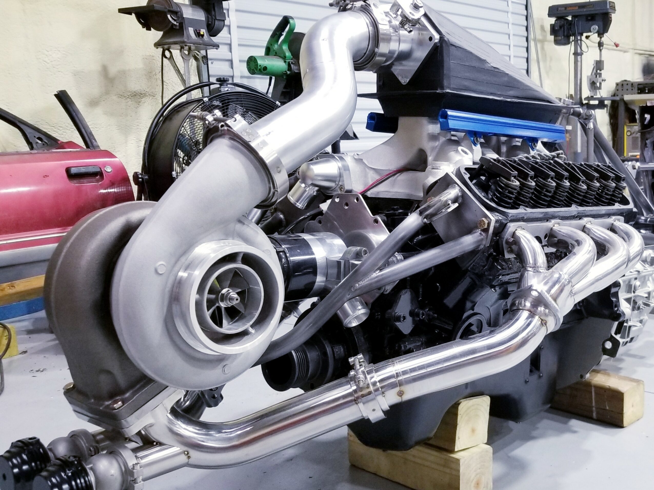 A large turbocharger connected to an engine with metal pipes and components in a workshop setting.