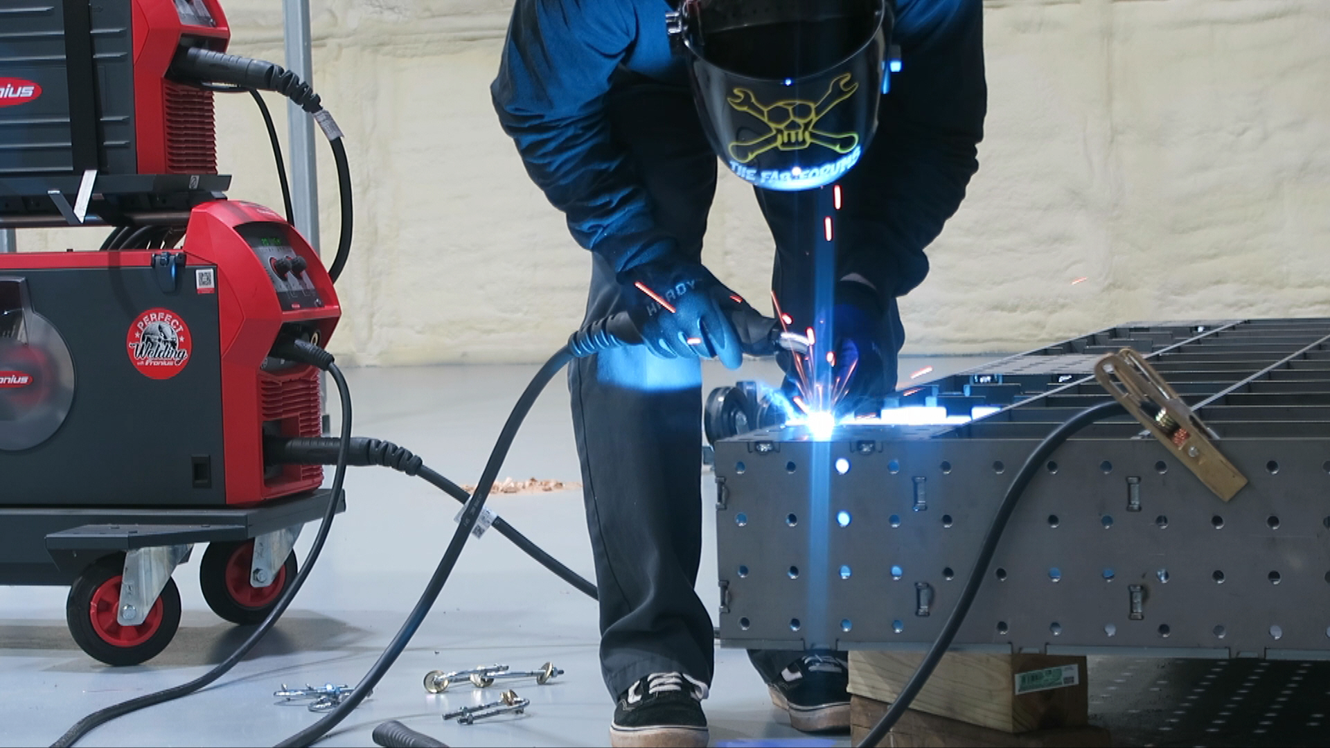 Person welding metal with bright sparks, wearing protective gear, next to welding equipment, on a workbench.