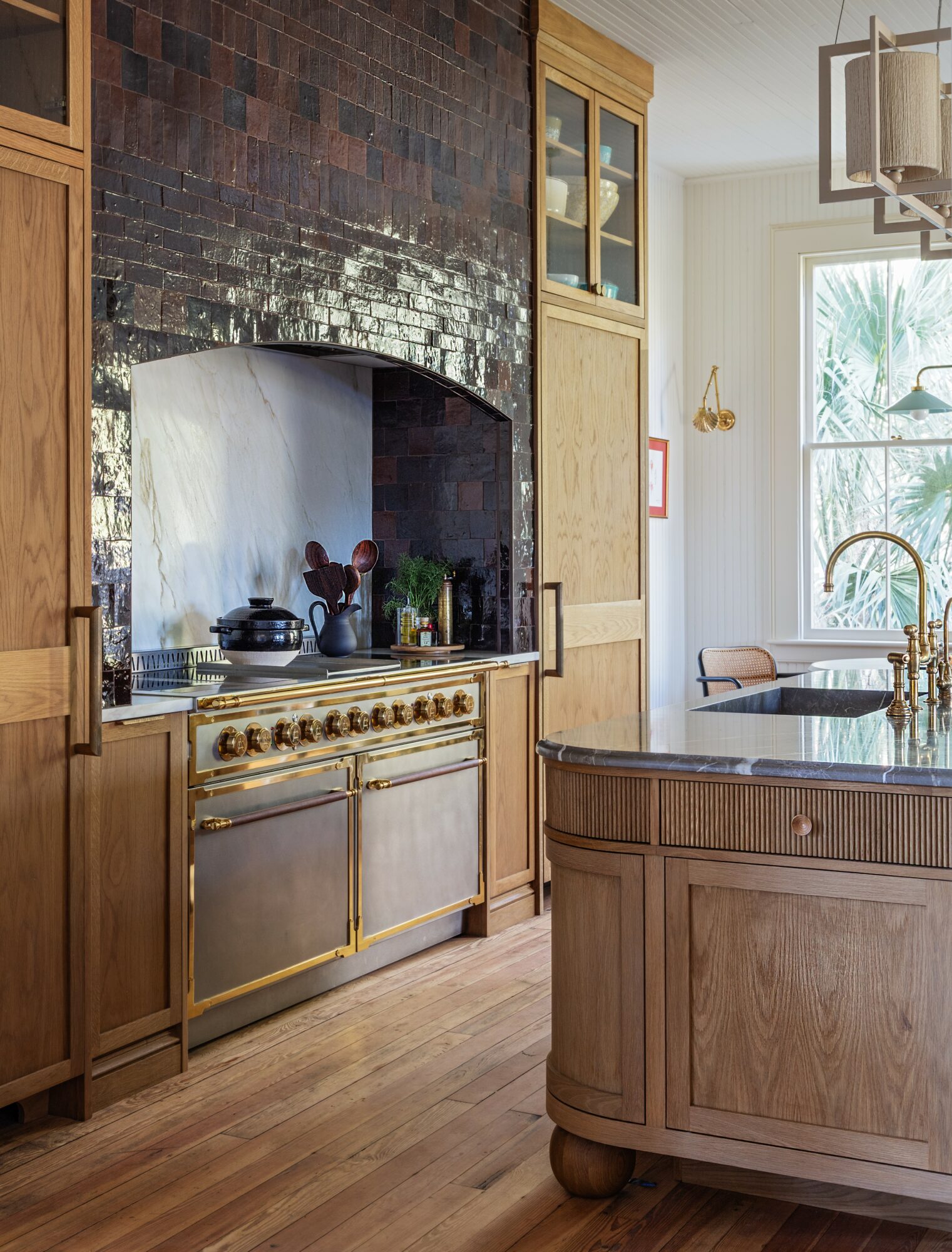Kitchen with brick oven, wooden cabinets, stainless steel appliances, and a curved island, illuminated by natural light from a window.