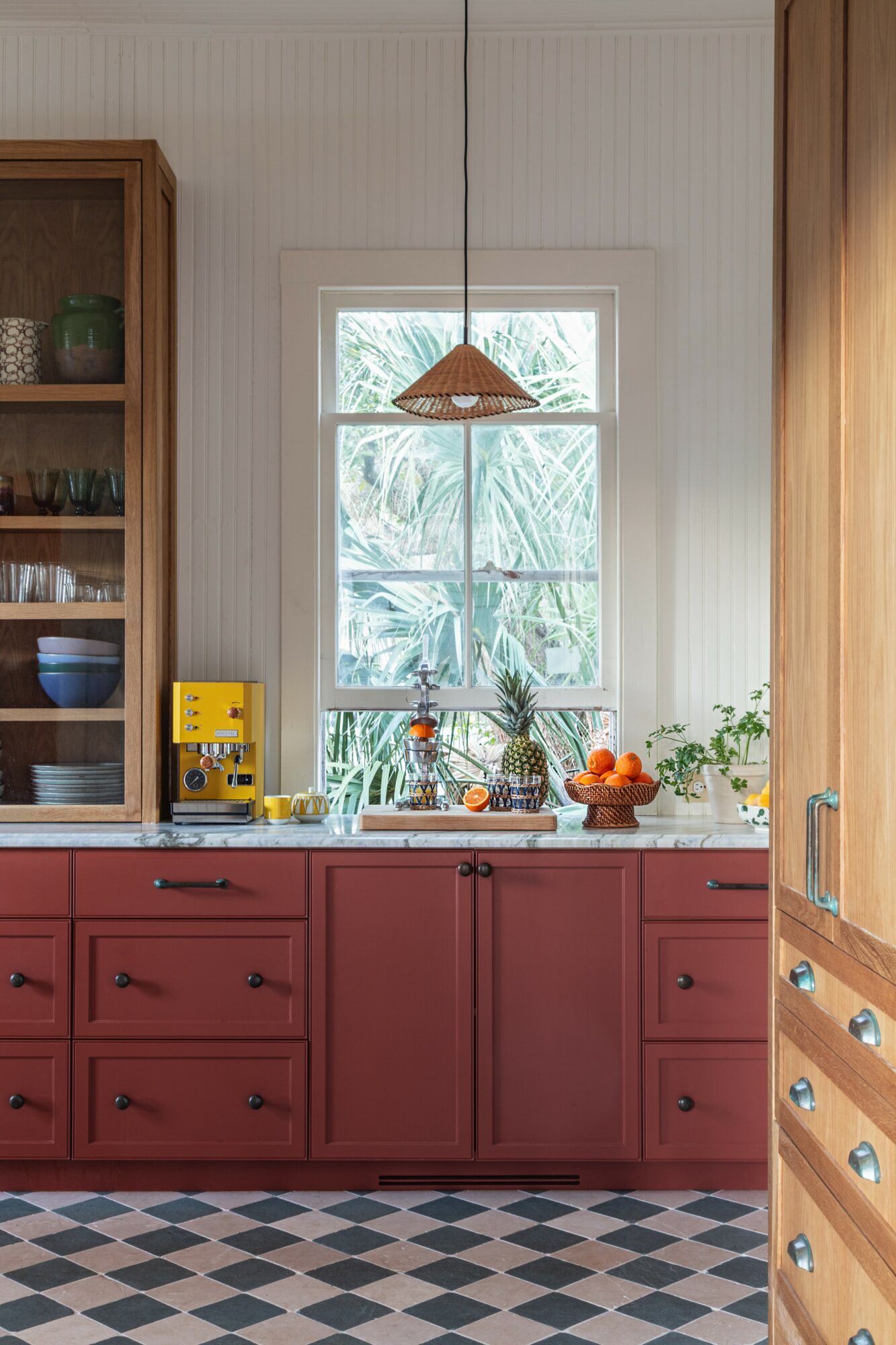 Kitchen window with plants and oranges on the counter, wooden cabinets, and patterned floor tiles.