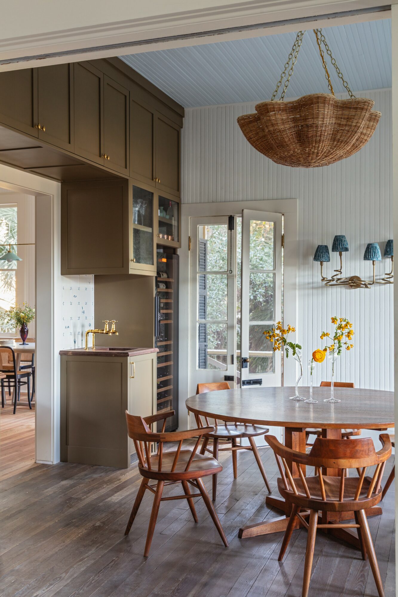 Dining area with wooden table, chairs, hanging basket, and open door to outside, bright and airy with natural light.