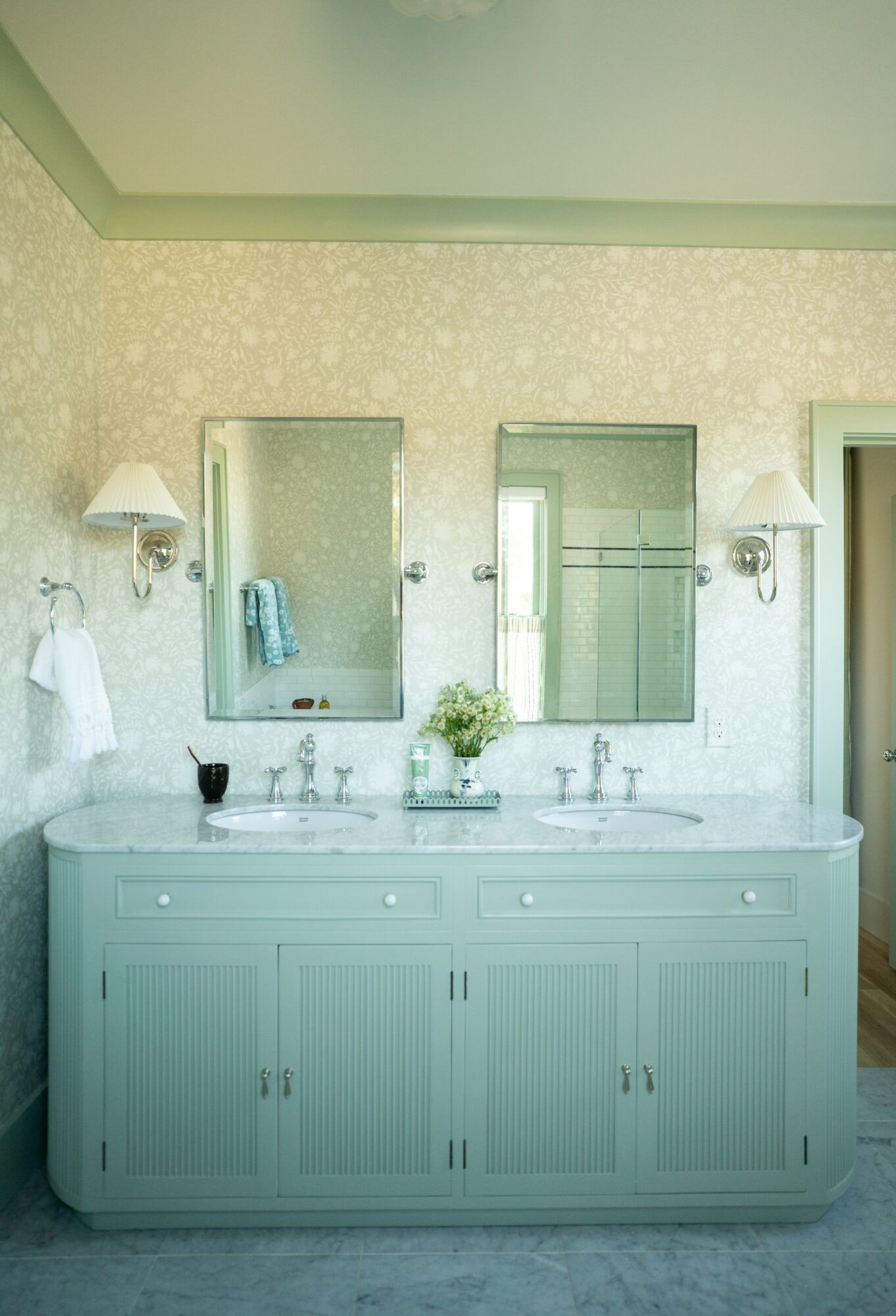 Bathroom vanity with two mirrors, wall-mounted lights, and a white cabinet with drawers and doors, against a patterned wall.
