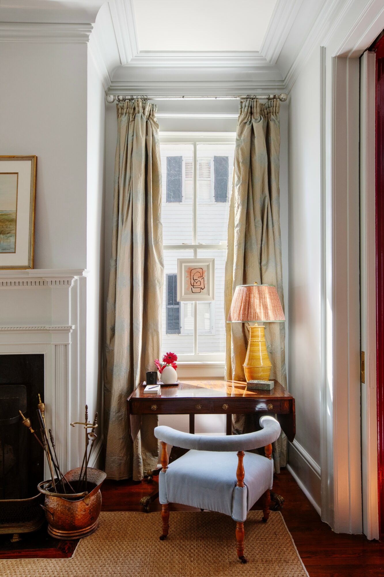 Interior window with curtains, table with lamp, and chair in a room corner, natural light streaming in.