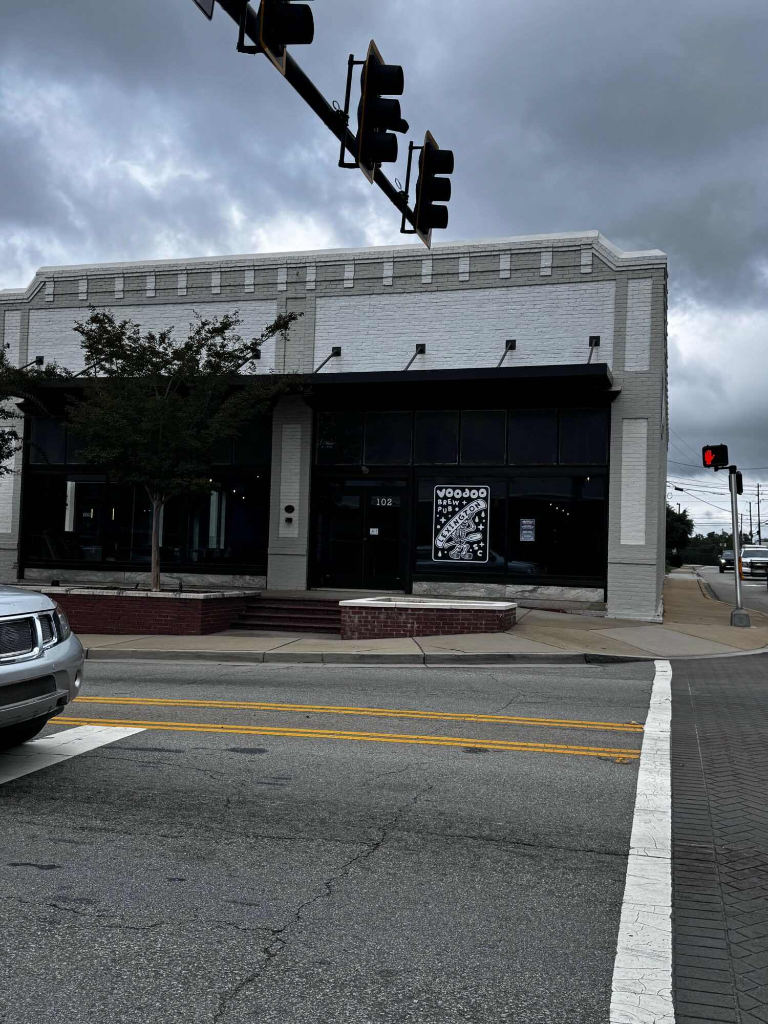 Street corner with traffic lights, building, and a parked car, under cloudy sky.