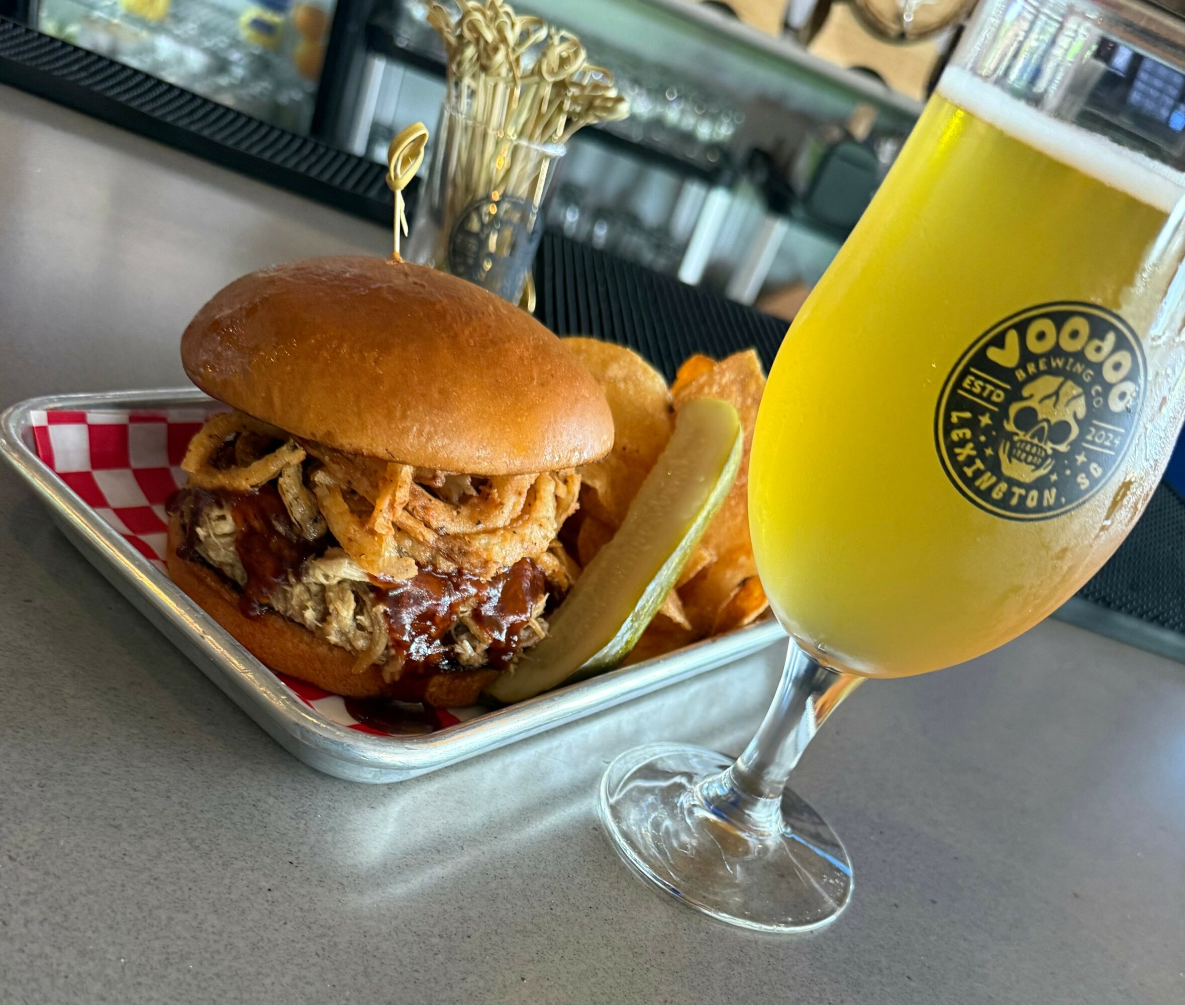 Burger with fried onions, fries, and a lemon wedge on a tray, with a glass of beer nearby.