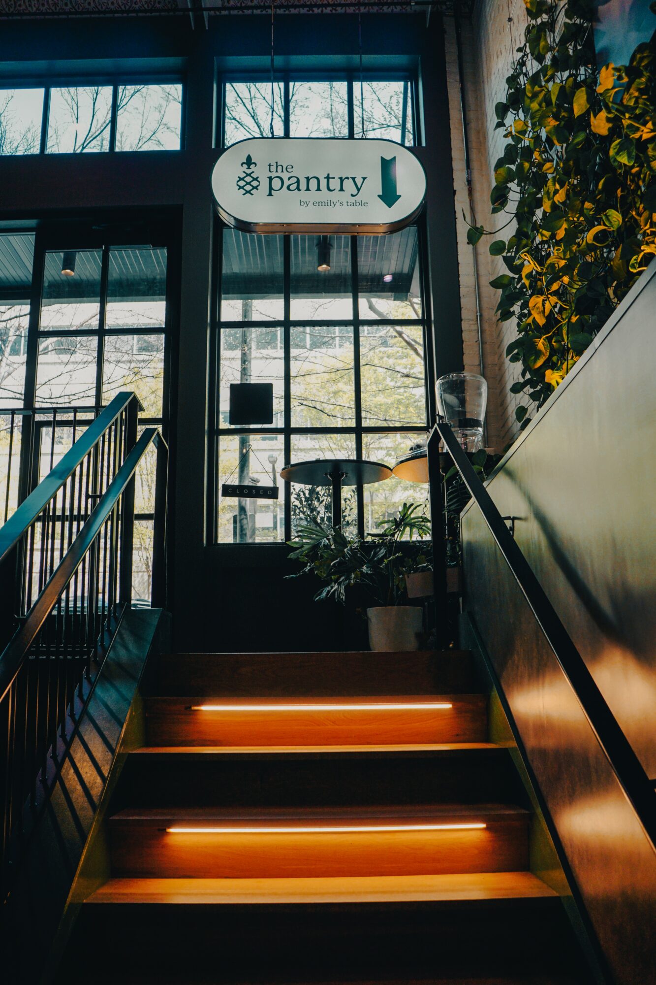 Indoor staircase leading to a door with a sign for the pantry, illuminated steps, and a window with trees outside.
