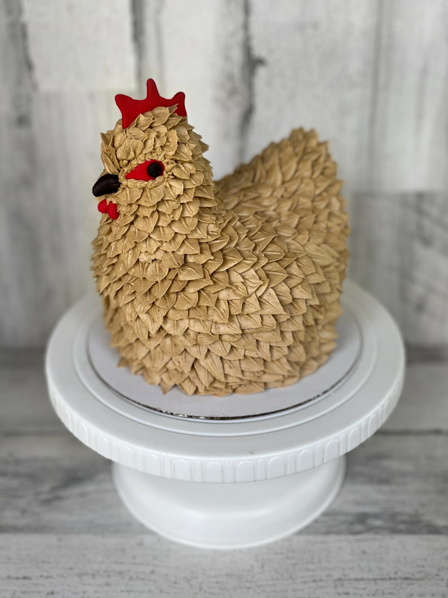 Decorative chicken-shaped figure with textured surface, red comb, and black eyes, placed on a white stand against a wooden background.
