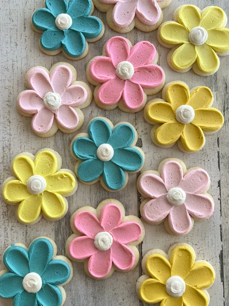 Colorful flower-shaped objects in pink, yellow, blue, and light pink with white centers on a wooden surface.