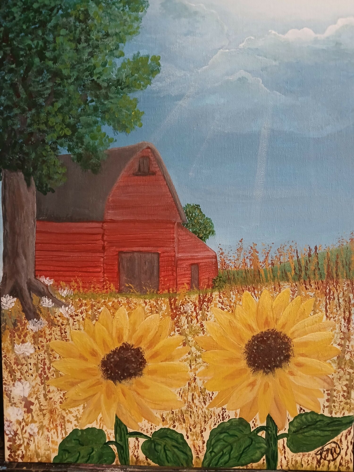 Red barn with sunflower field, green trees, blue sky, and clouds in background.