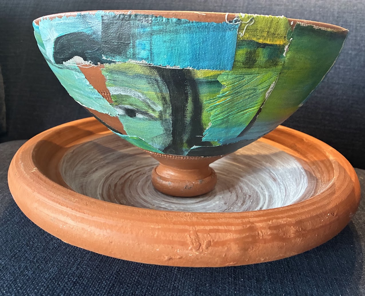 Decorative bowl with colorful abstract design on a wooden stand, placed on a dark surface.