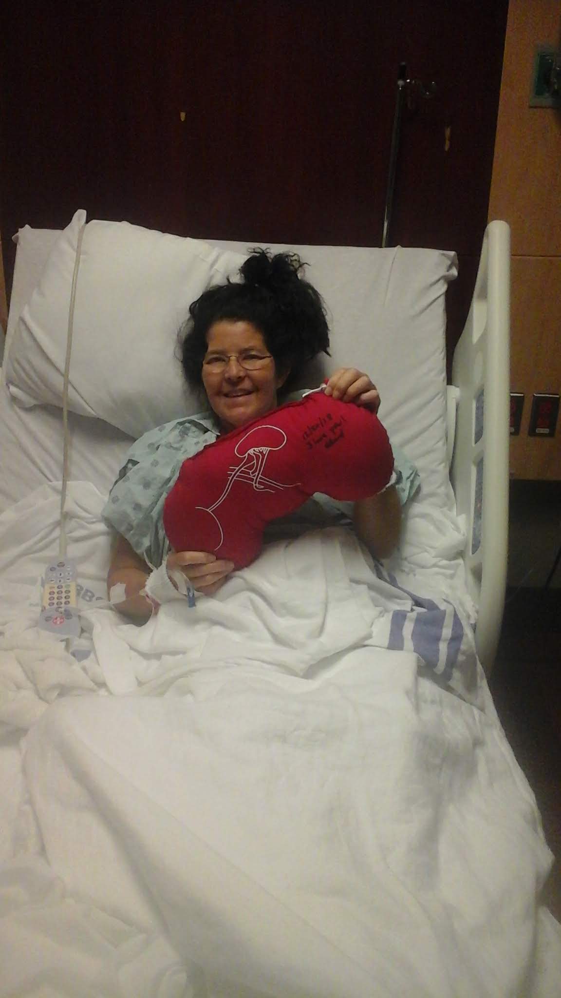 Child lying in hospital bed holding a red heart-shaped balloon, smiling, with medical equipment nearby.