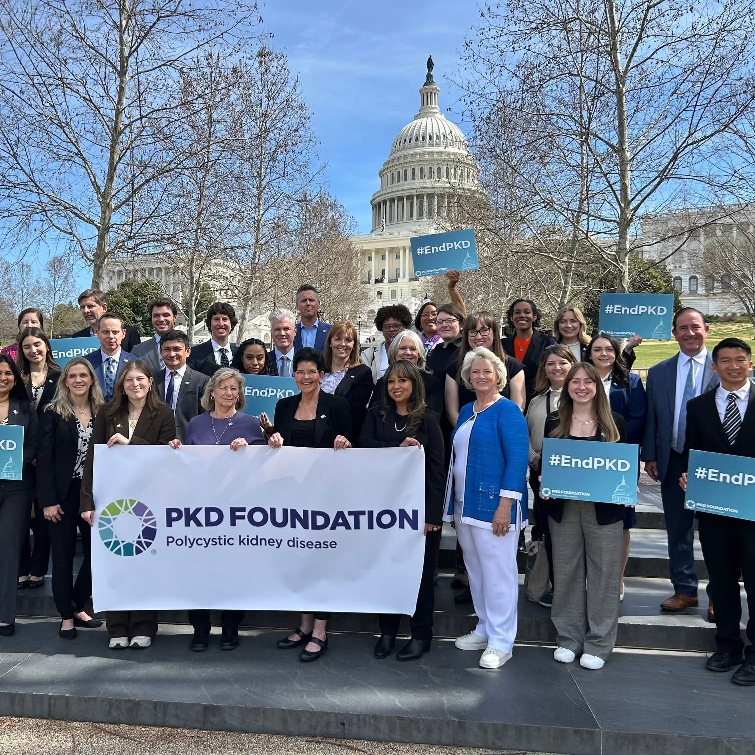 Group of people holding a banner and signs in front of the U.S. Capitol building, promoting PKD Foundation and polycystic kidney disease.