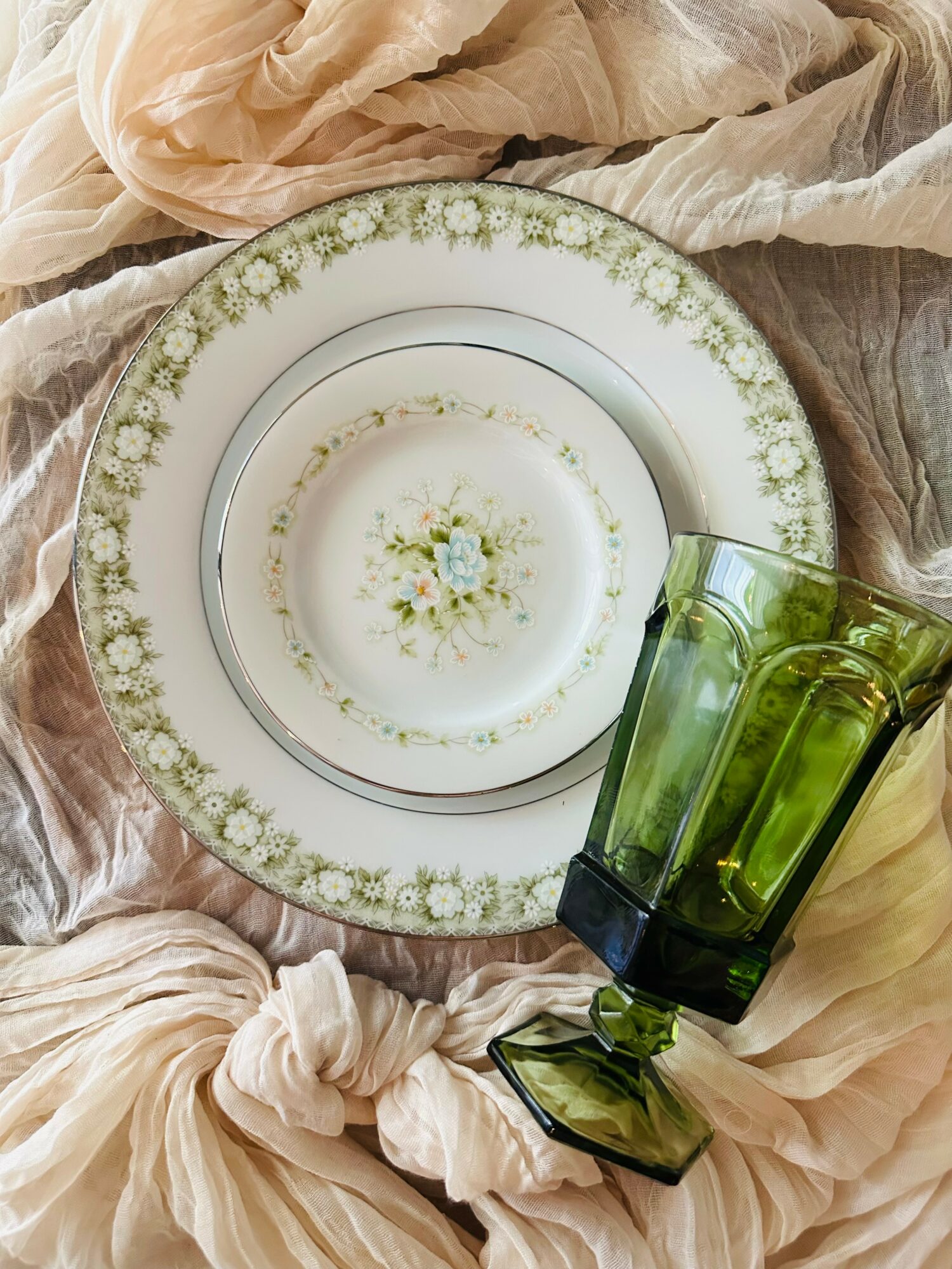 A decorative plate with floral patterns, a green glass, and soft fabric in the background.