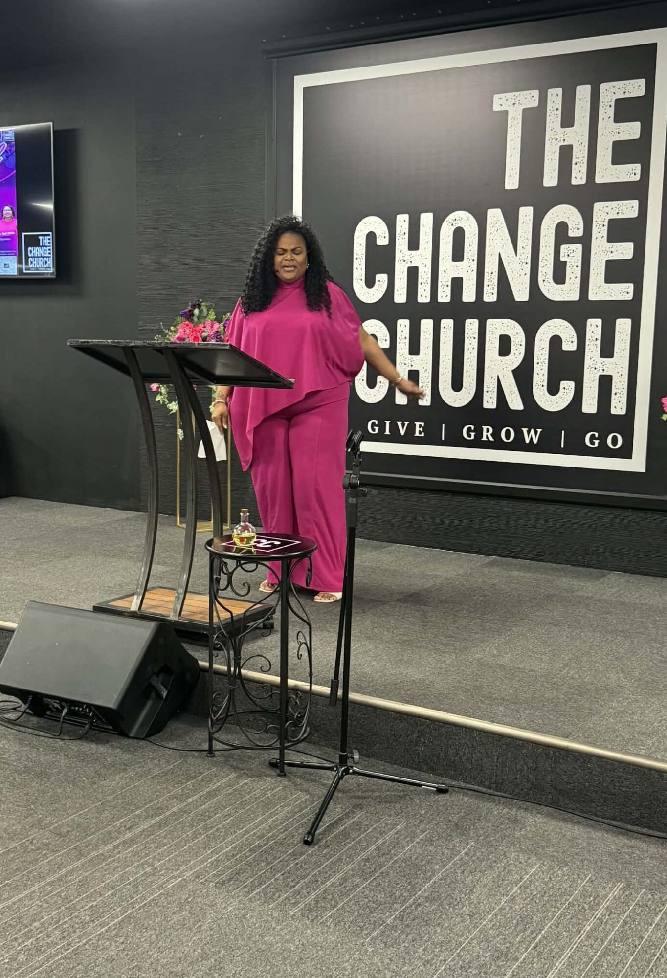 Woman in pink dress standing at a podium in front of a large sign that reads 'THE CHANGE CHURCH'.