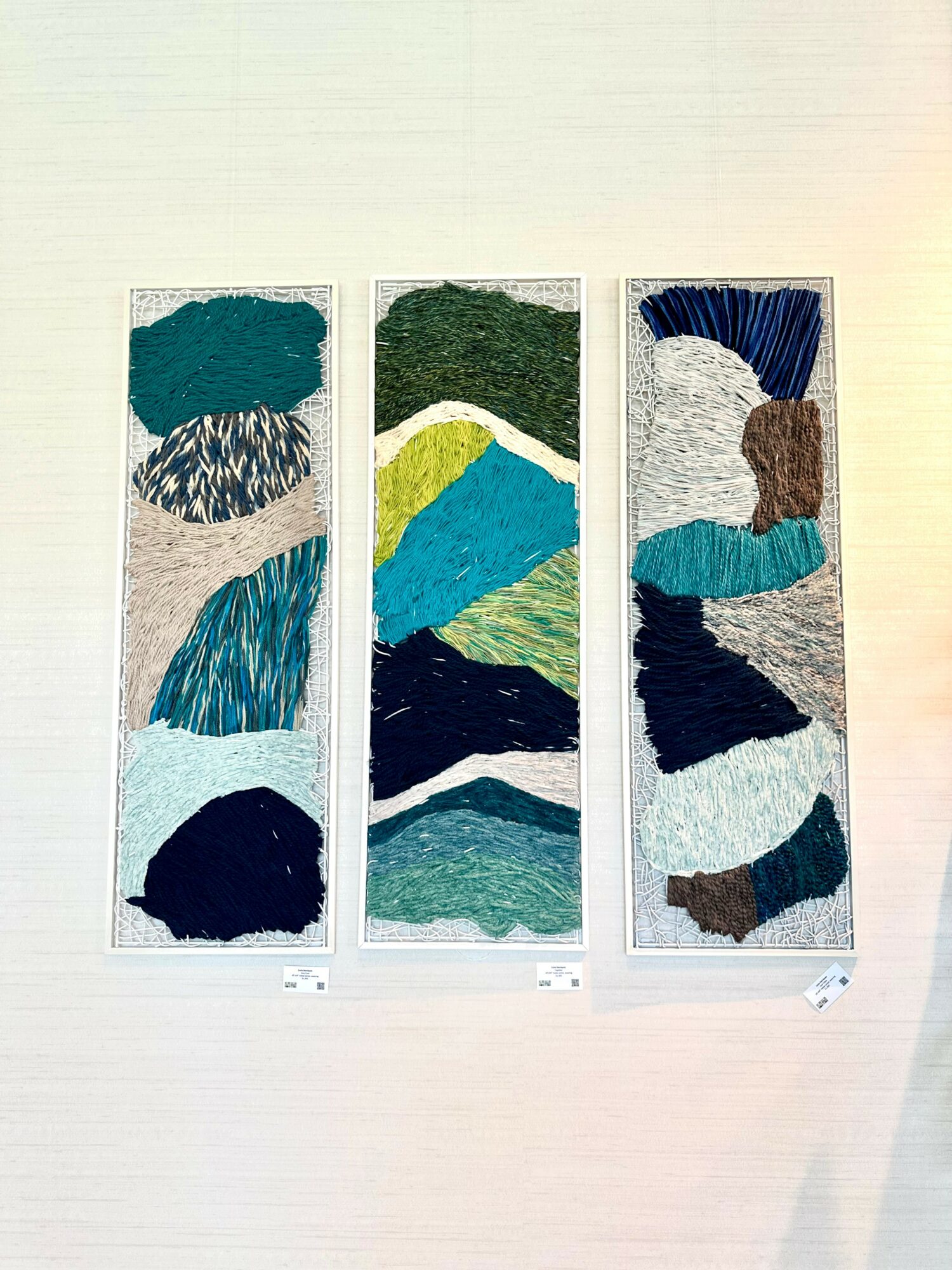 Three vertical textile art panels with abstract landscape designs, featuring blue, green, yellow, and brown colors.