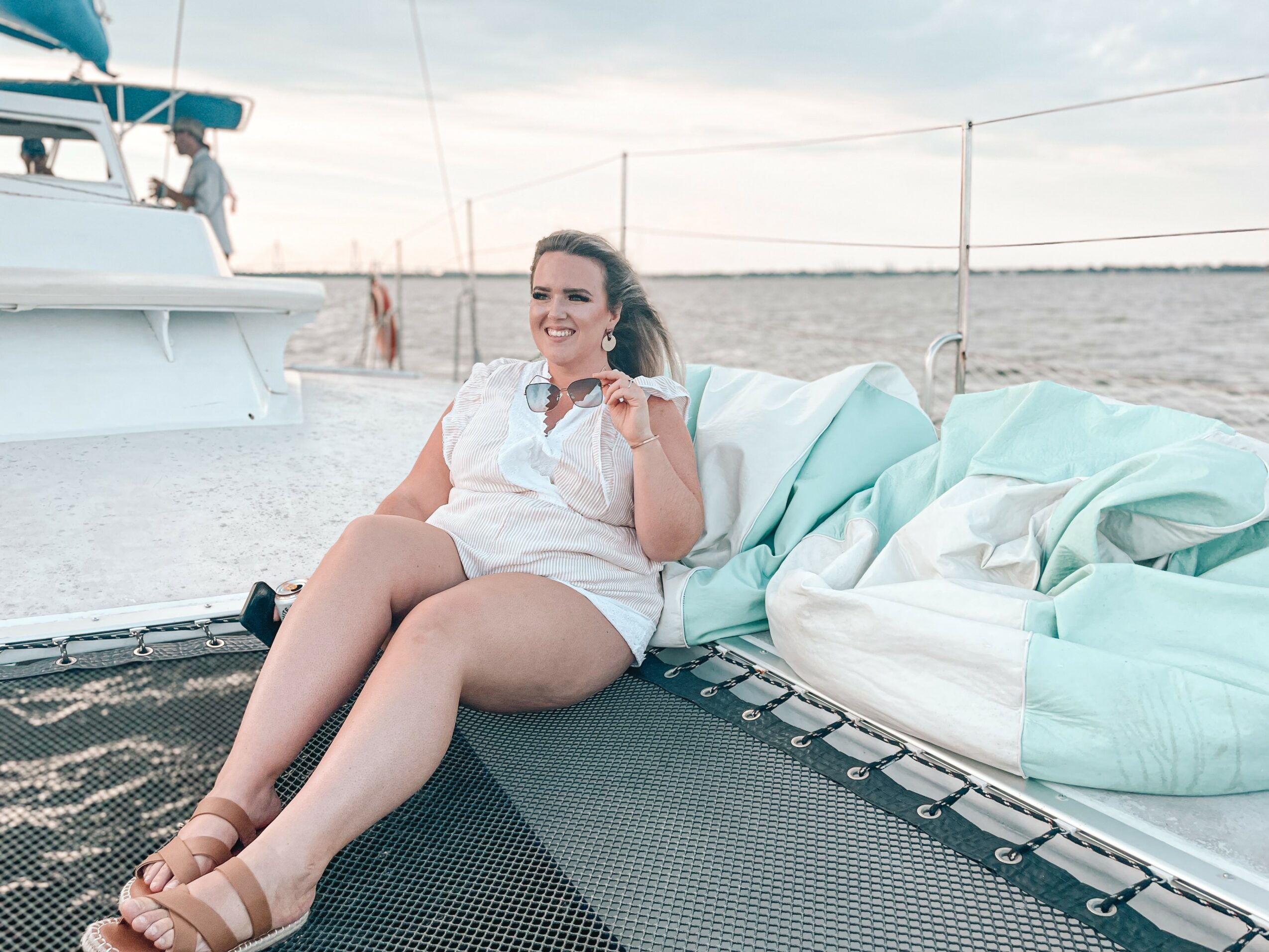 Woman sitting on a trampoline on a boat, smiling, with a body of water in the background.