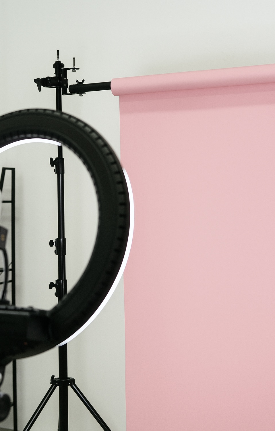 Photography backdrop with a pink sheet and a lighting stand, partially visible, against a plain wall.